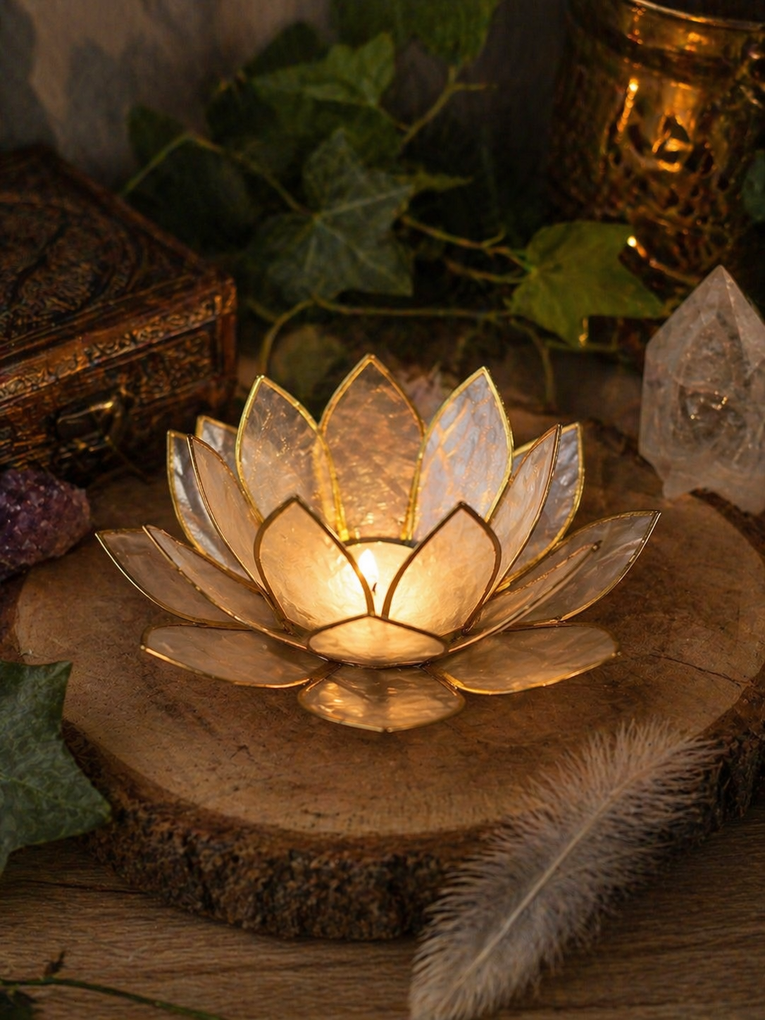 Photophore lotus nacré doré allumé sur tranche de bois, ambiance chaleureuse avec lierre en fond.