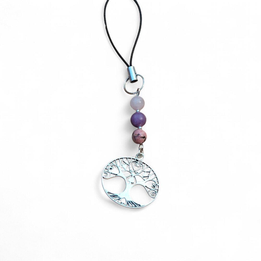 Bijou de téléphone arbre de vie avec kunzite, lépidolite et rhodonite sur fond clair, création Magic Gaïa aux tons rose mauve, douceur et apaisement.