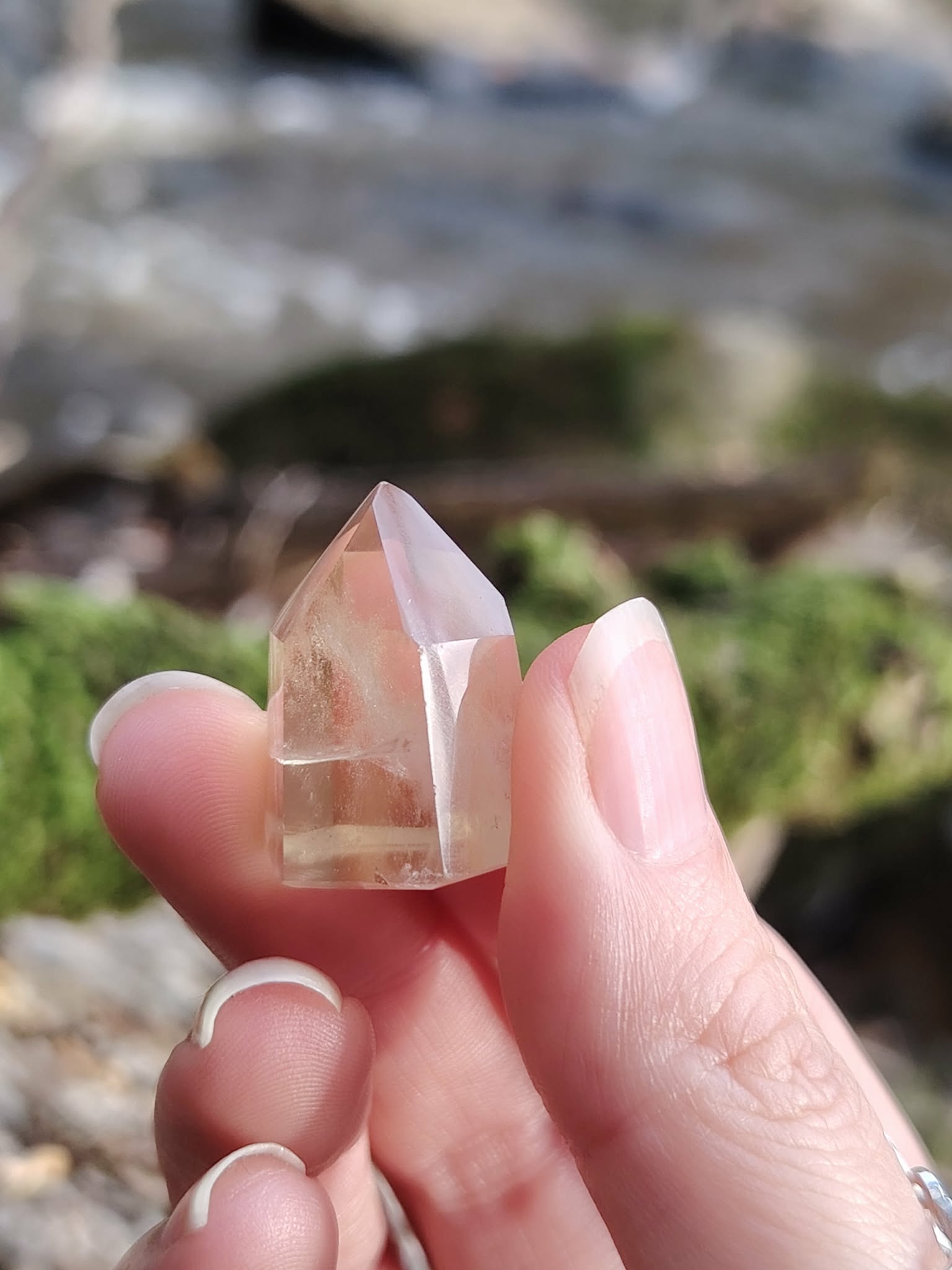Pointe citrine naturelle tenue entre les doigts en lumière naturelle, petit cristal poli jaune clair, motivation, joie et vitalité.