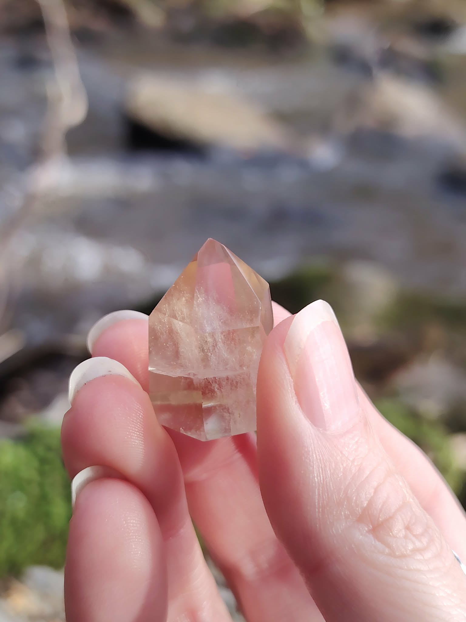 Pointe citrine naturelle entre les doigts en gros plan, petit cristal poli lumineux aux reflets dorés, bonne humeur, assurance et énergie solaire.