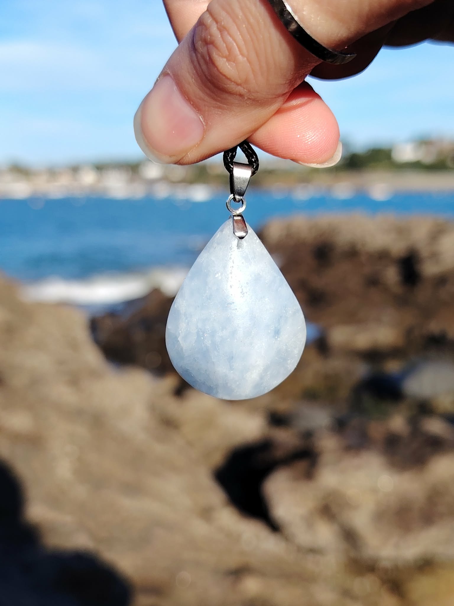 Pendentif calcite bleue naturelle en gros plan sur cordon noir, pierre polie bleu nuageux, détente intérieure et communication douce.