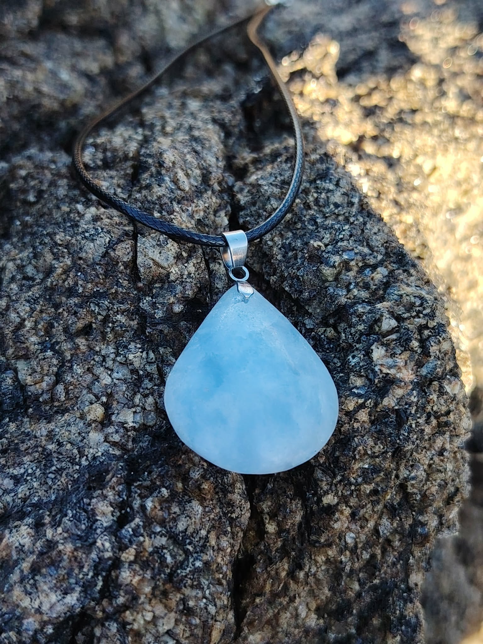 Pendentif calcite bleue naturelle présenté en extérieur sur bois brut en Bretagne, pierre goutte bleu laiteux, apaisement et équilibre émotionnel.