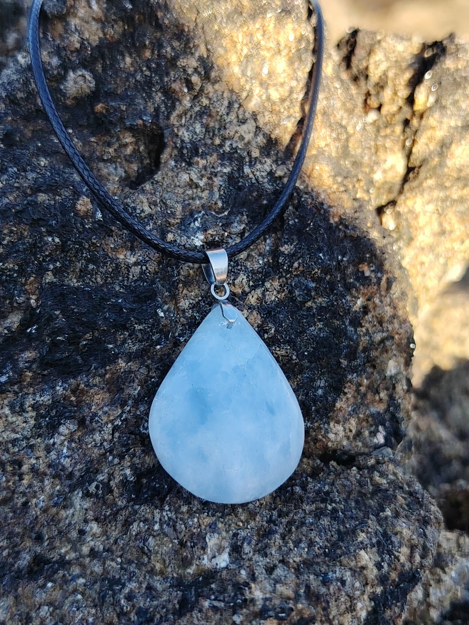 Pendentif calcite bleue naturelle porté sur cordon noir en lumière naturelle, pierre goutte bleu tendre, communication apaisée et douceur émotionnelle.