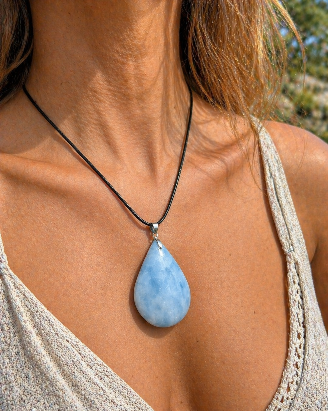 Pendentif calcite bleue naturelle porté sur cordon noir en lumière naturelle, goutte bleu pastel, calme intérieur et douceur émotionnelle.