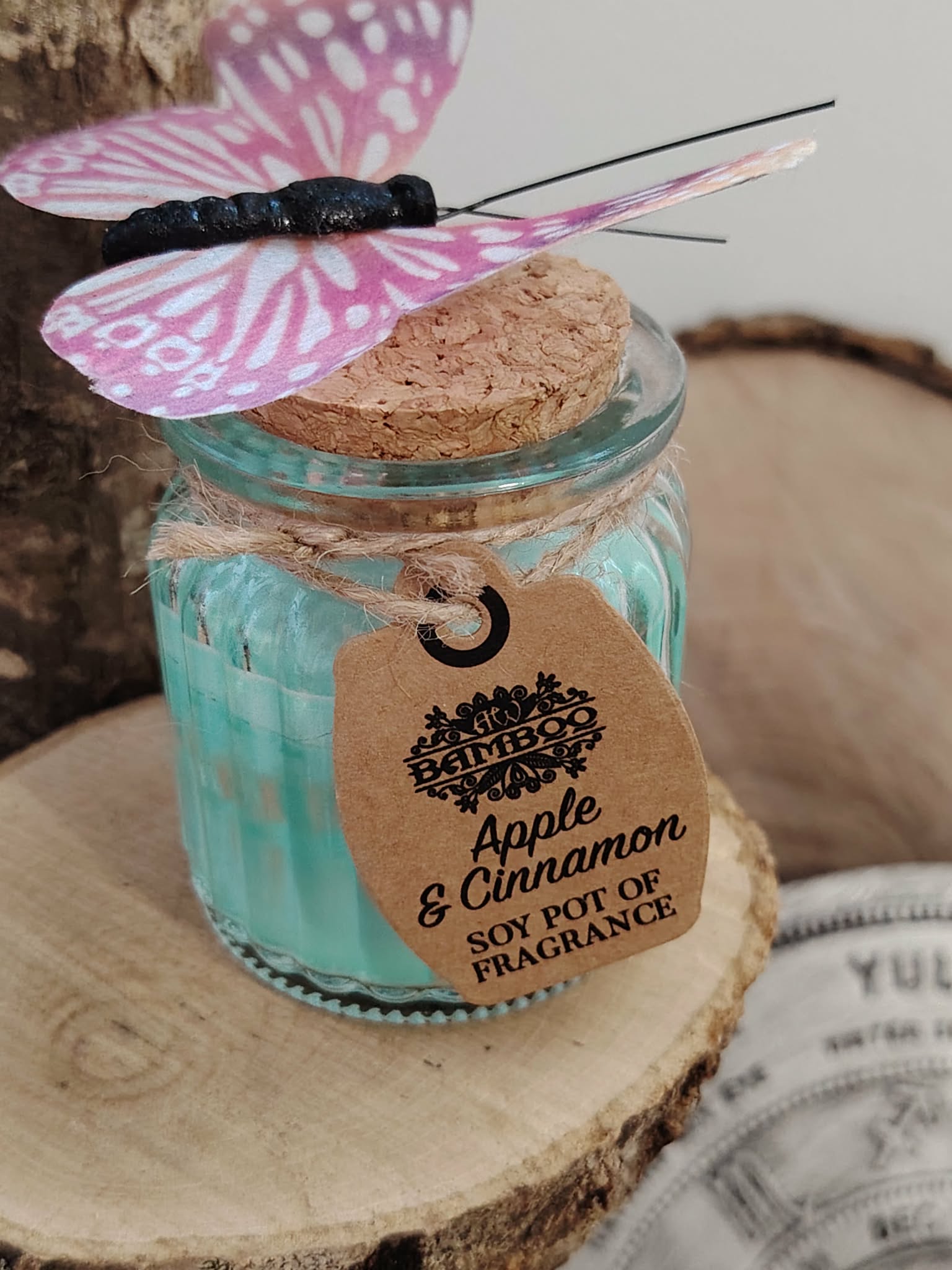 Bougie parfumée Pomme Cannelle en pot en verre sur tranche de bois avec papillon décoratif, cire de soja naturelle et atmosphère douce.