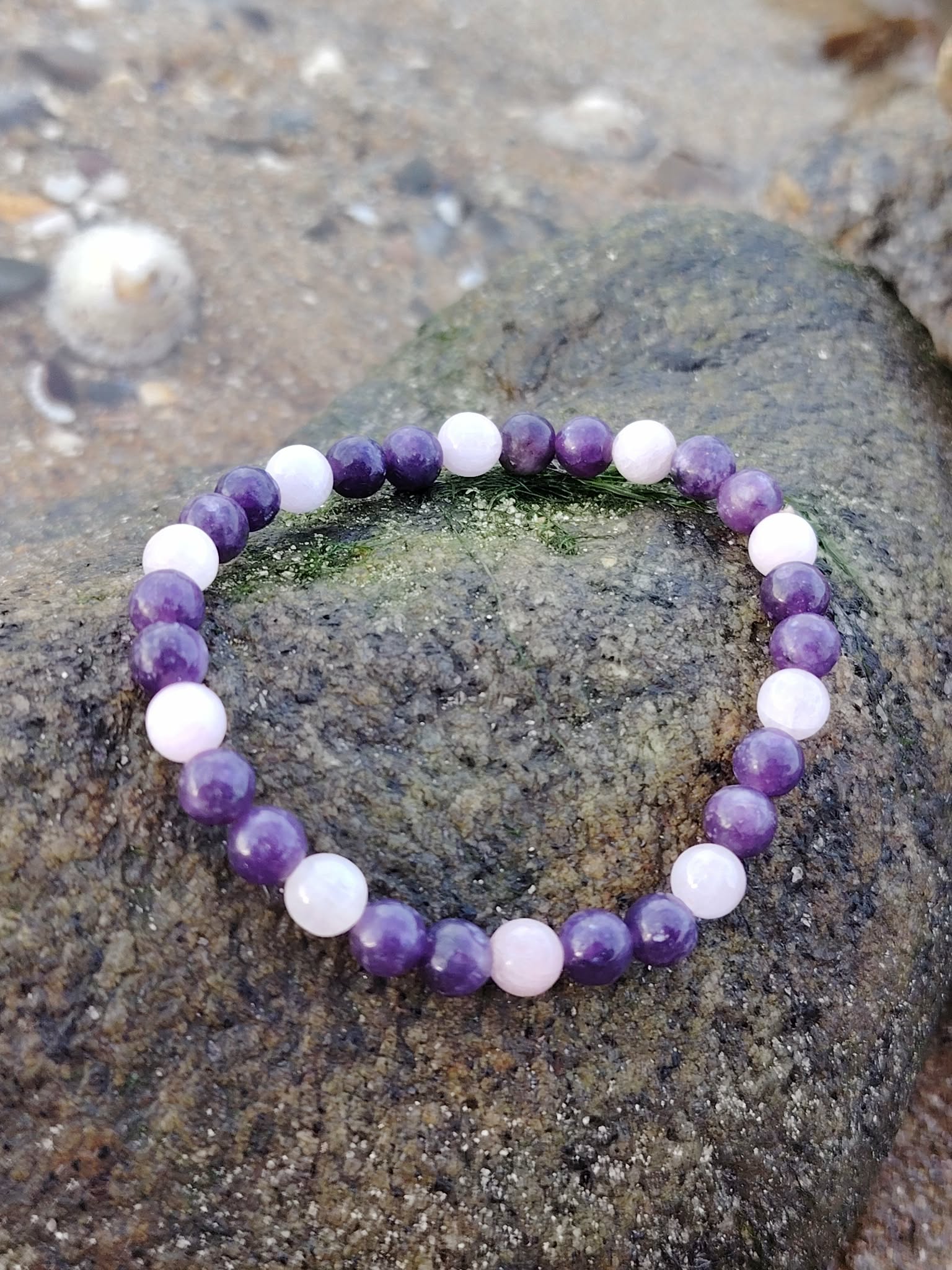 Bracelet Lépidolite Kunzite en pierres naturelles sur roche bretonne, mélange de perles mauves et roses, douceur émotionnelle et sérénité.
