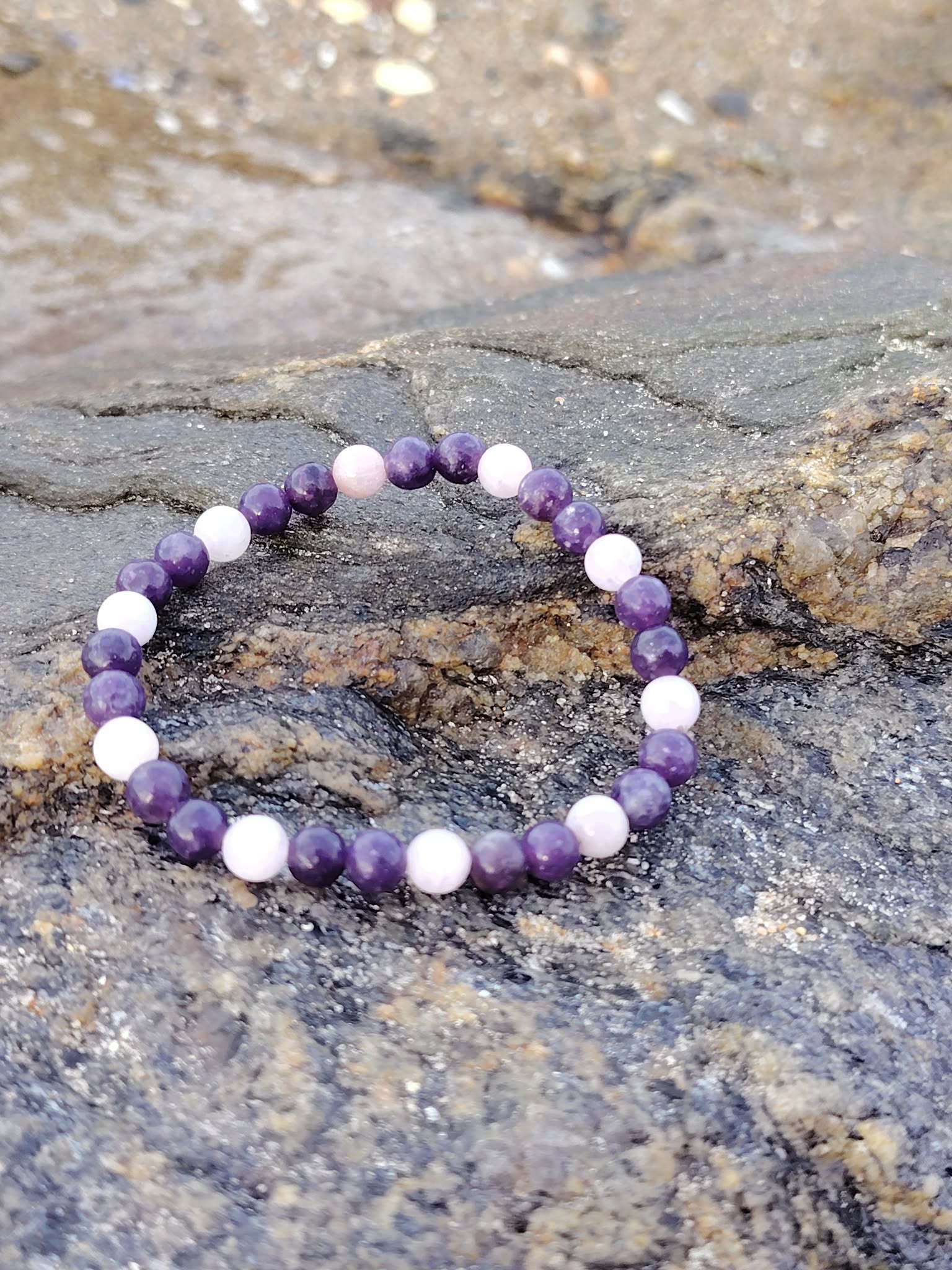Bracelet Kunzite Lépidolite sur rocher en bord de mer en Bretagne, perles 6 mm violettes et rosées, apaisement et paix intérieure.