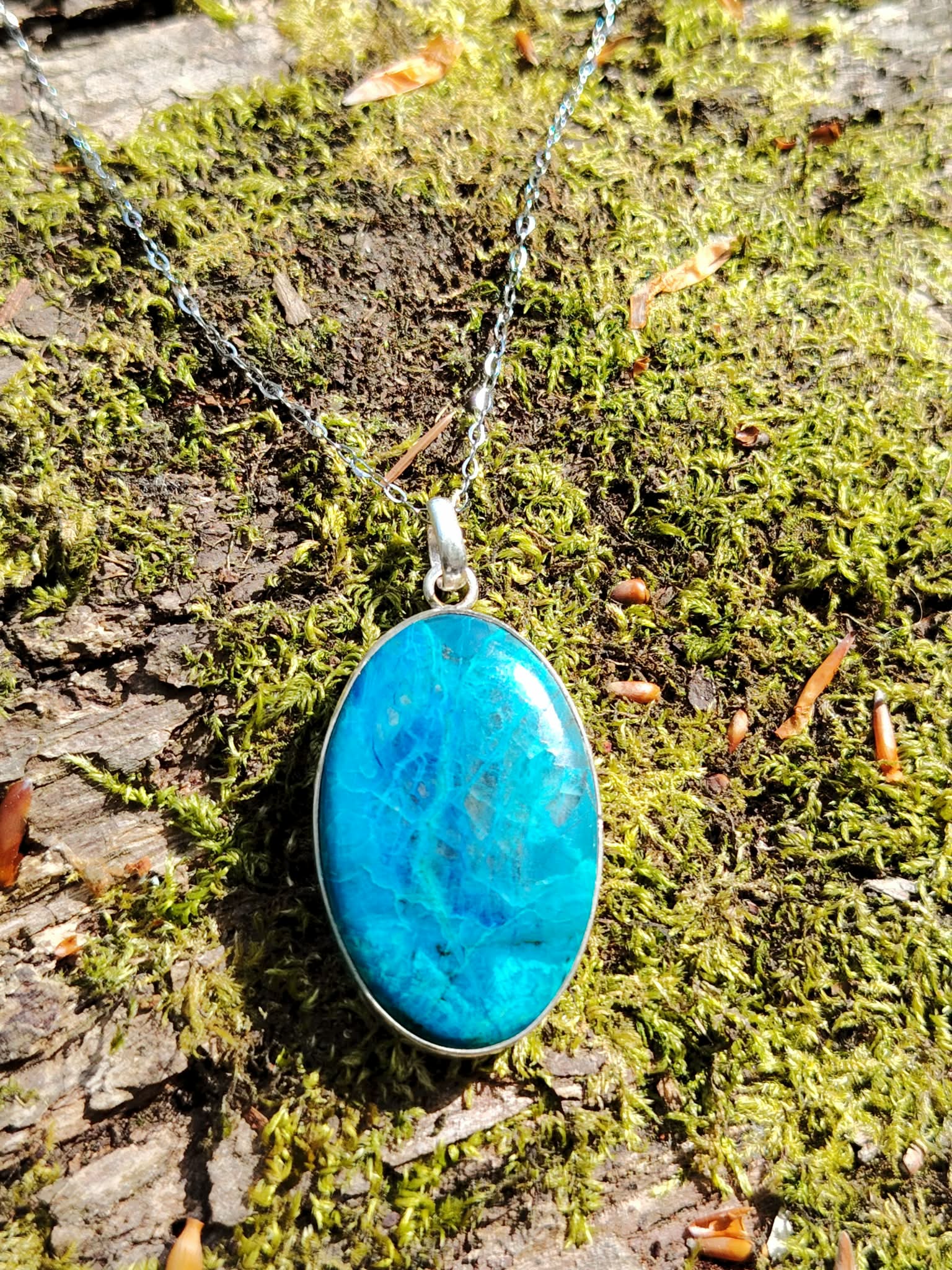 Pendentif chrysocolle argent 925 sur chaîne posé sur mousse en forêt, pierre ovale bleu turquoise naturelle, recentrage et apaisement du cœur.