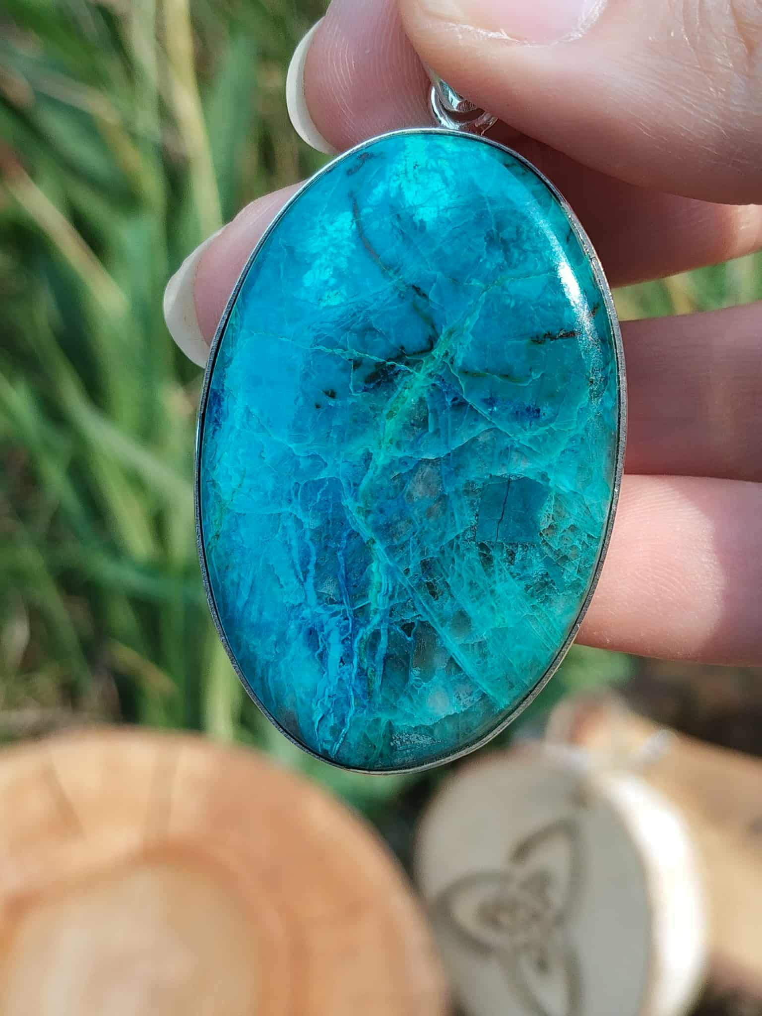 Gros plan sur pendentif chrysocolle argent 925 tenu entre les doigts, pierre bleu vert lumineuse, sérénité émotionnelle et communication authentique.