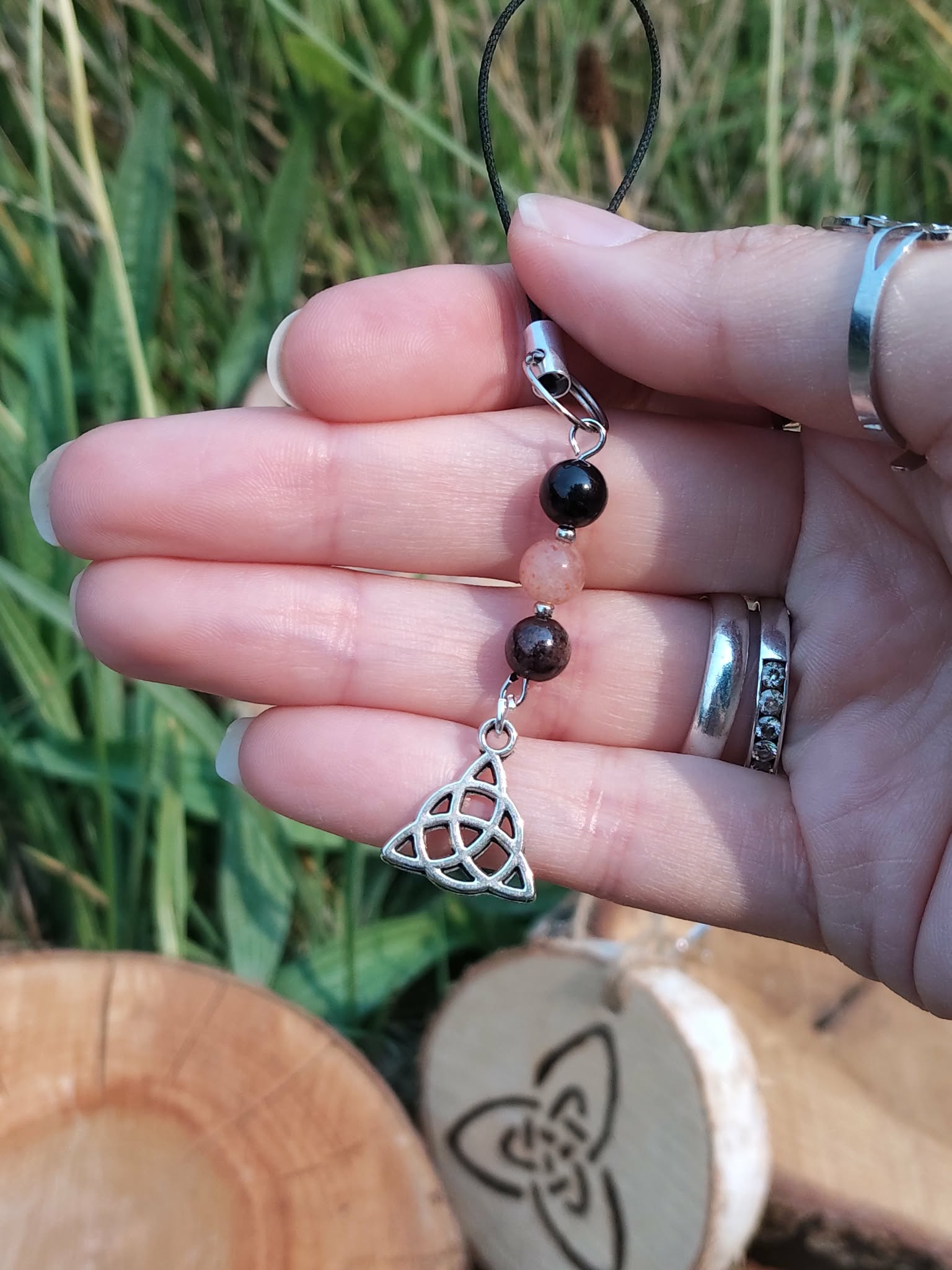 Bijou de téléphone Viking Triquetra en mise en situation naturelle, perles noires et rose tendre, harmonie et protection symbolique.