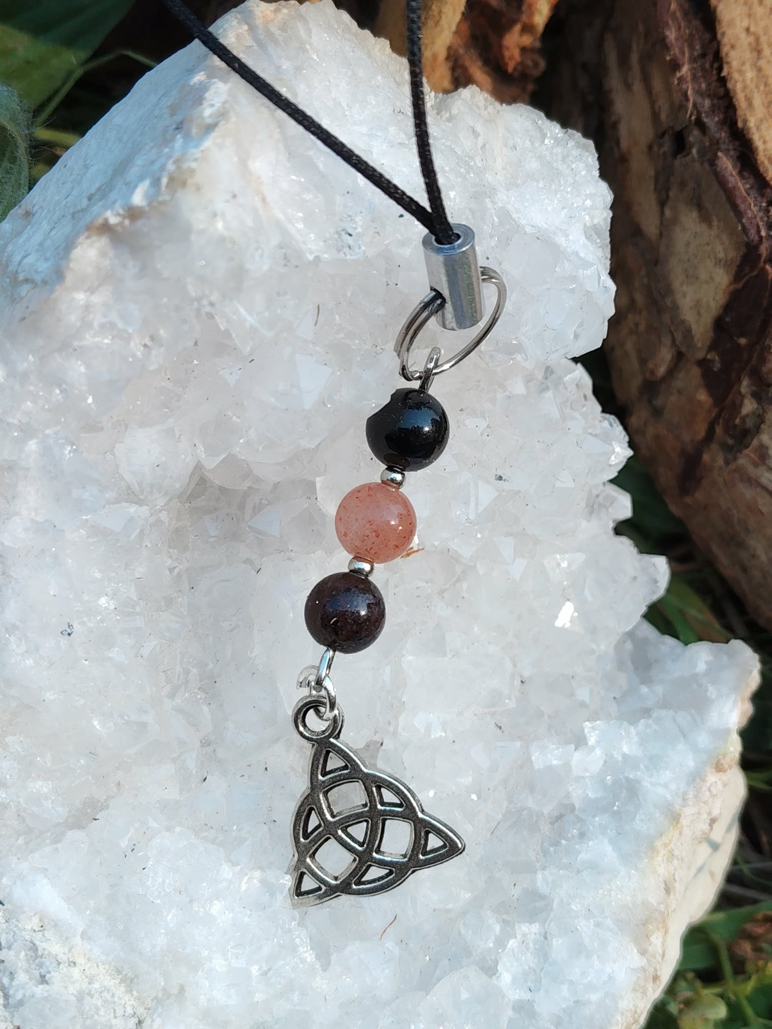 Bijou de téléphone avec symbole Triquetra argenté, perles noires, roses et détails métalliques, ancrage et sérénité.