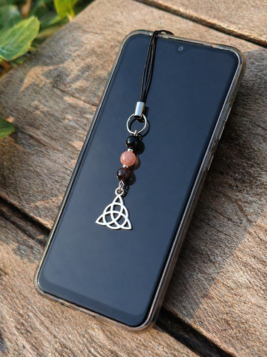 Bijou de téléphone Triquetra fixé sur smartphone, perles noires brillantes et perle rose poudré avec pendentif argenté, équilibre émotionnel, douceur et protection.