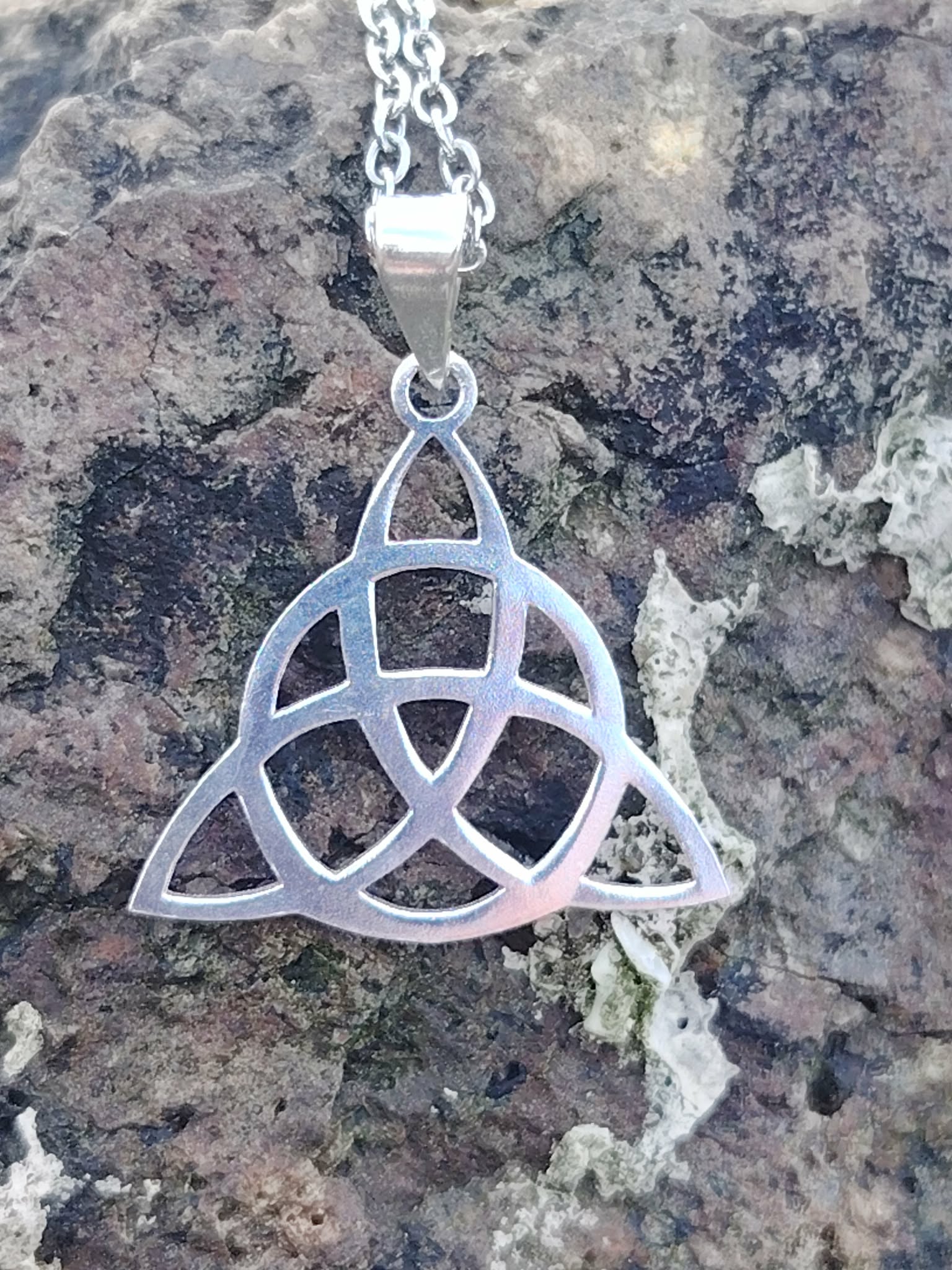 Pendentif Triquetra en argent 925 posé sur bois naturel en extérieur, bijou celtique ajouré avec chaîne argentée, harmonie, protection et équilibre intérieur.
