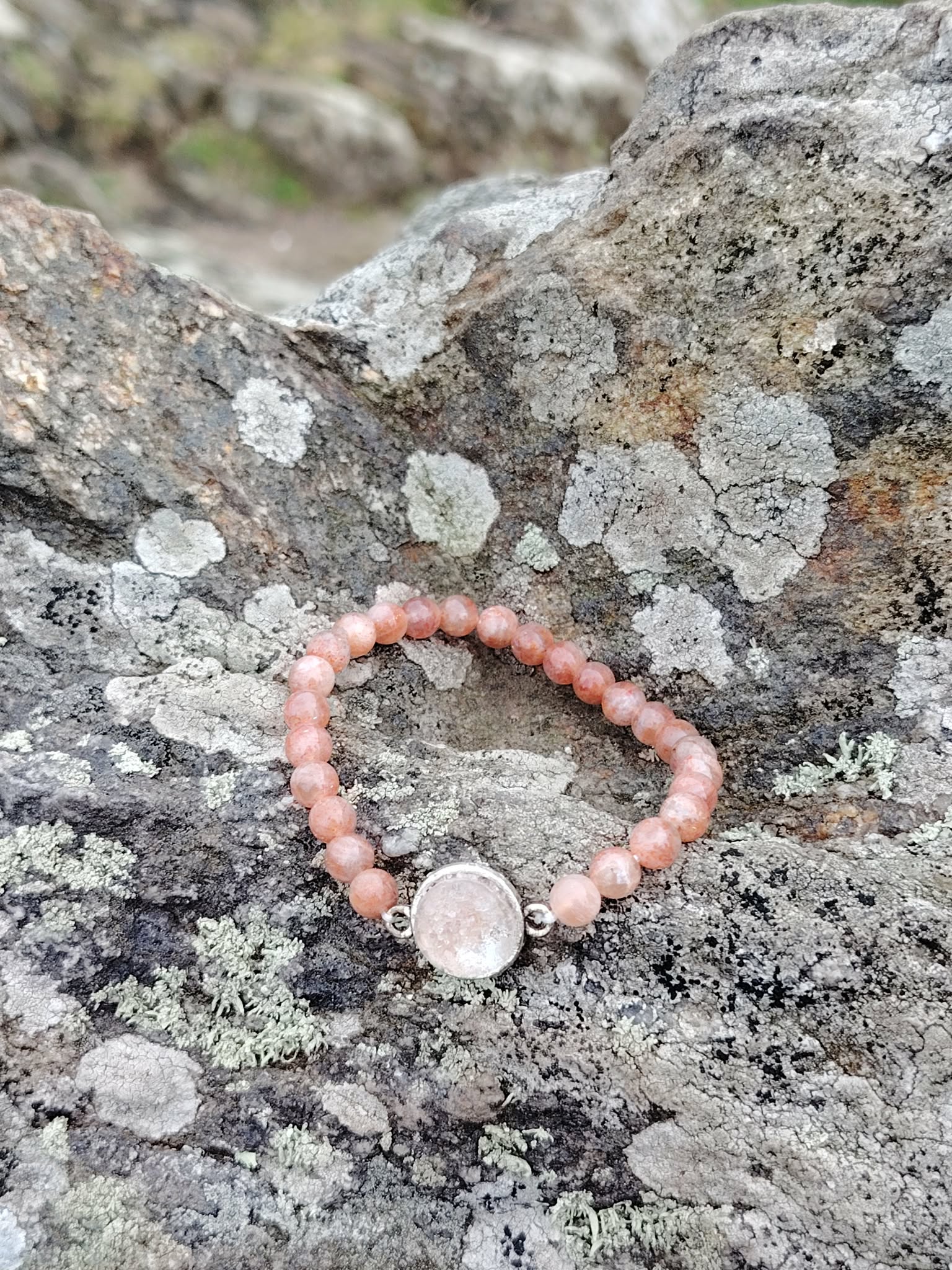 Bracelet pierre de soleil femme sur pierre naturelle en bord de mer breton, bijou énergétique aux tons saumon cuivrés, vitalité, motivation et chaleur intérieure.