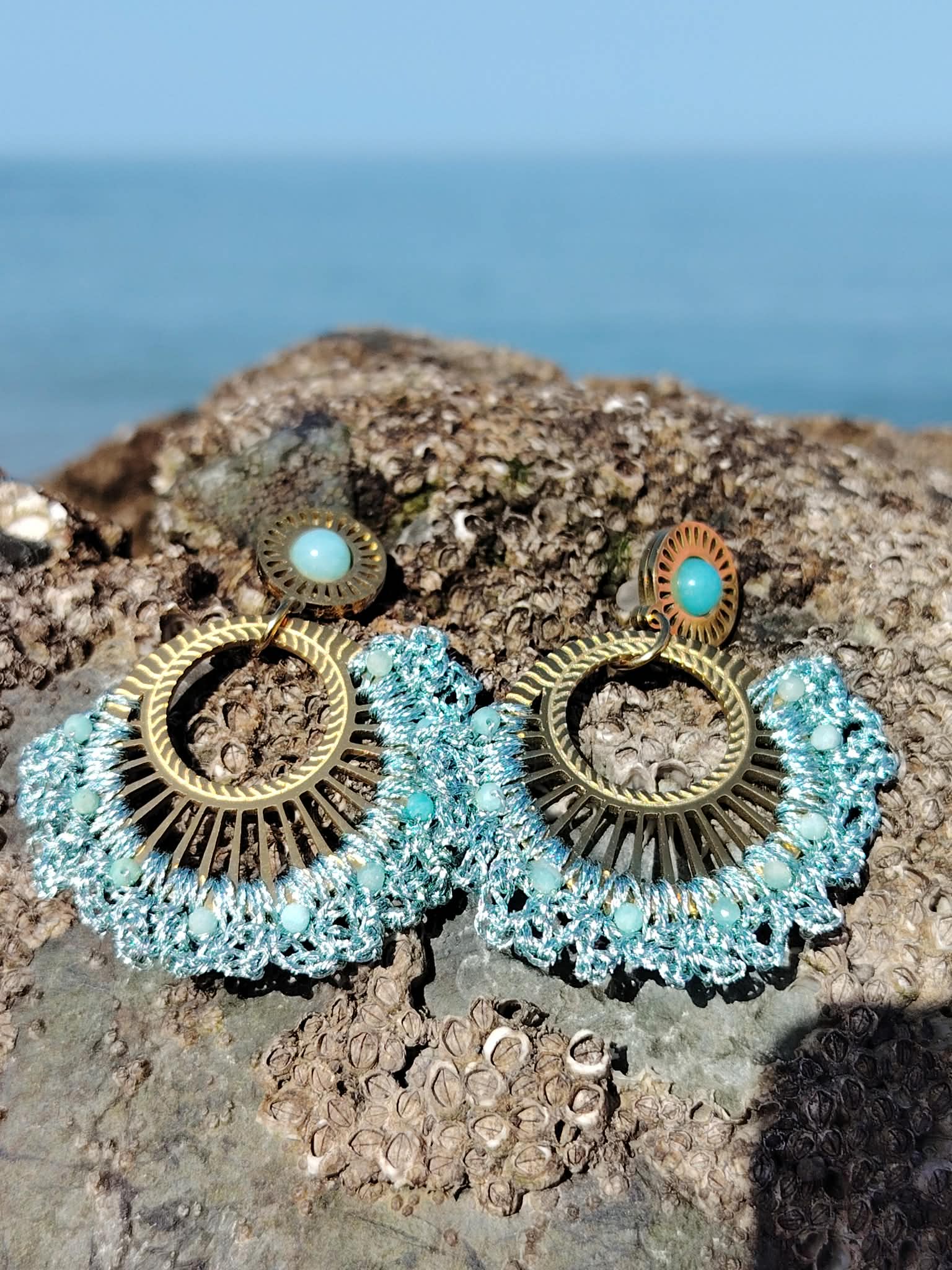 Boucles d’oreilles pendantes dorées éventail tissé avec pierre bleu turquoise sur fond clair, bijou bohème chic lumineux et élégant