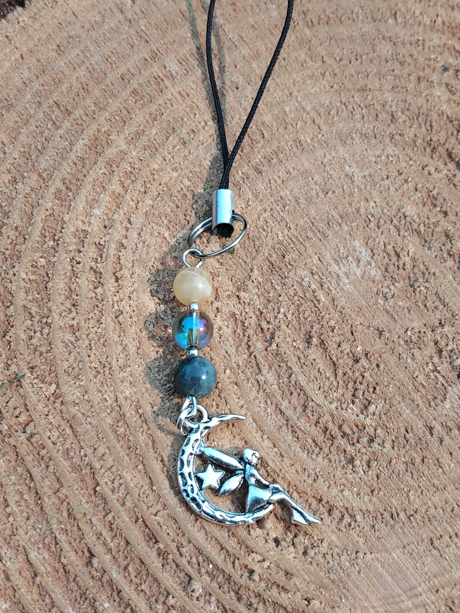 Bijou de téléphone féerique avec lune argentée sur fond de tranche de bois, détail des pierres naturelles et cordon noir