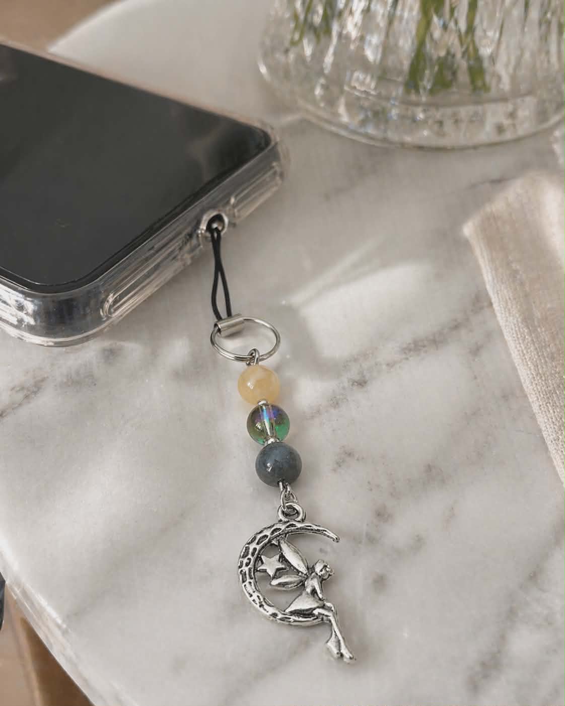 Bijou de téléphone Lune Féerique avec pierres naturelles et élément central irisé, une création élégante et poétique qui associe la beauté de la nature à une touche lumineuse et raffinée.