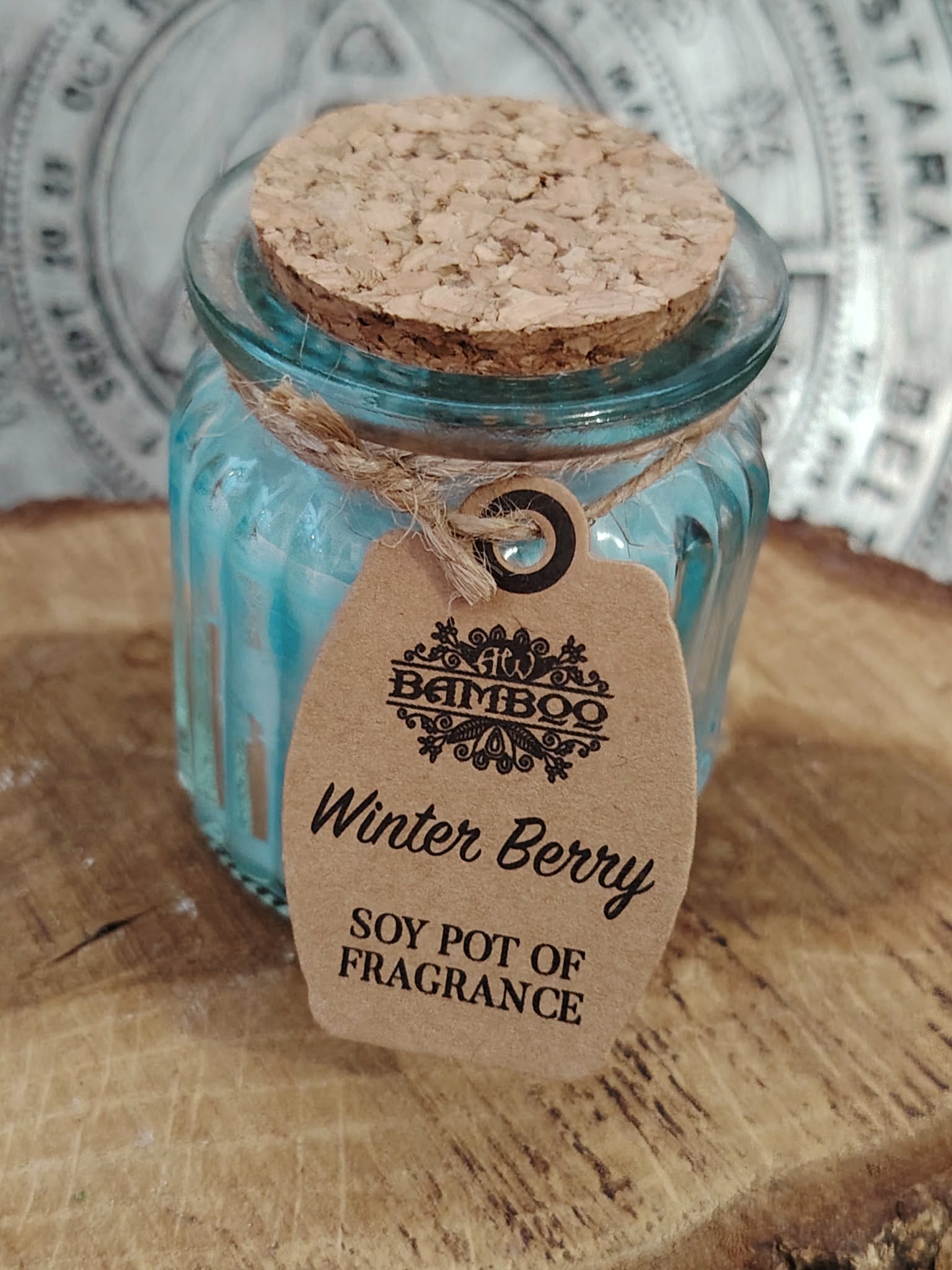 Bougie parfumée Baies d’Hiver en cire de soja dans pot en verre bleu avec couvercle en liège, posée sur tranche de bois