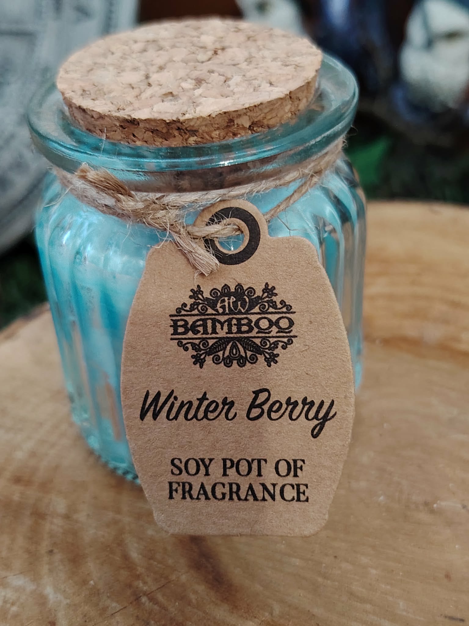 Zoom sur bougie parfumée Baies d’Hiver en cire de soja avec étiquette Winter Berry, pot en verre bleu et couvercle en liège