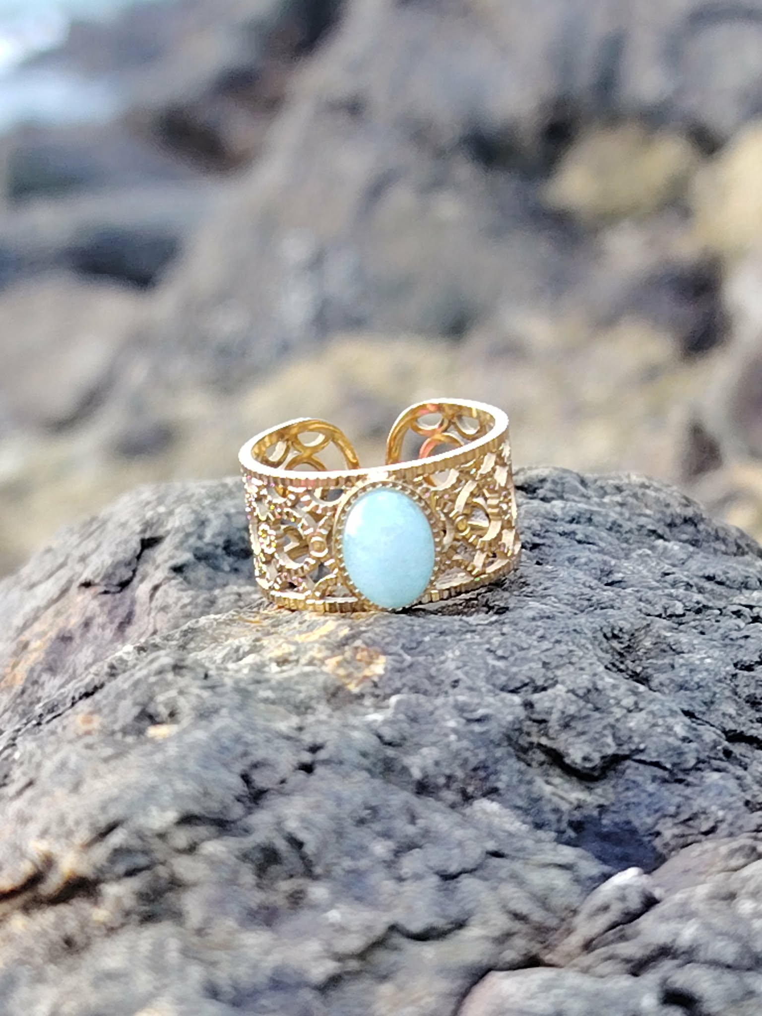 Bague réglable Amazonite photographiée sur la côte bretonne, cabochon ovale bleu-vert, acier inoxydable doré et allure bohème chic.