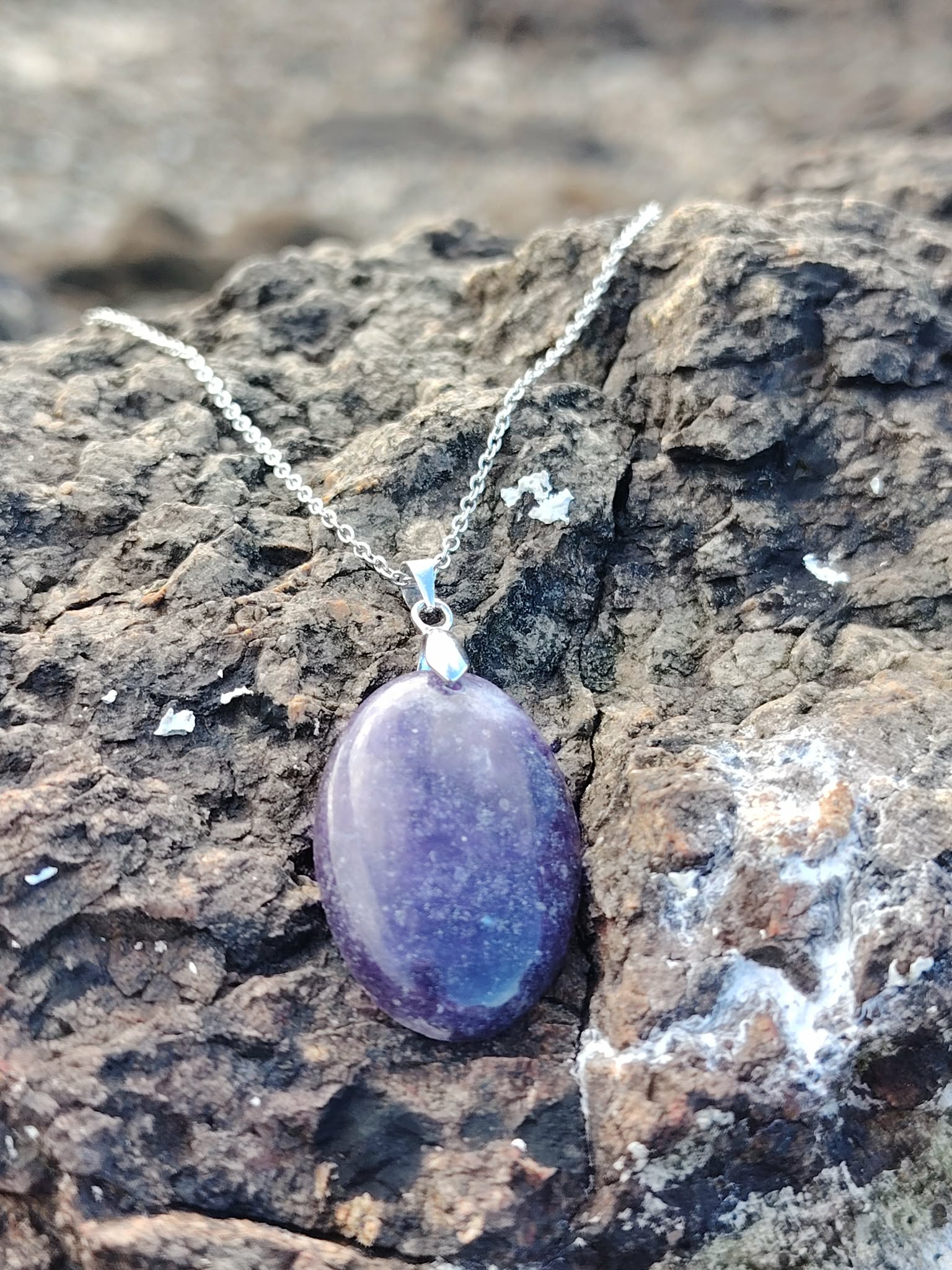 Pendentif Lépidolite ovale violette posé sur roche brute en Bretagne, pierre naturelle de calme intérieur, de transition douce et de bien-être émotionnel