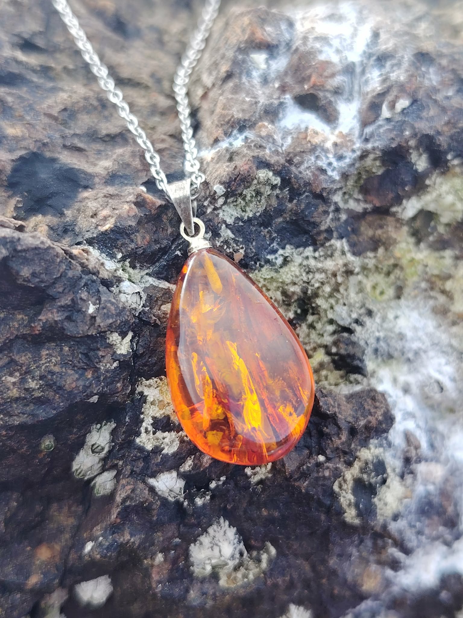 Pendentif Ambre baltique goutte sur roche en Bretagne, résine fossile miel orangé avec chaîne argentée, chaleur intérieure et vitalité douce.