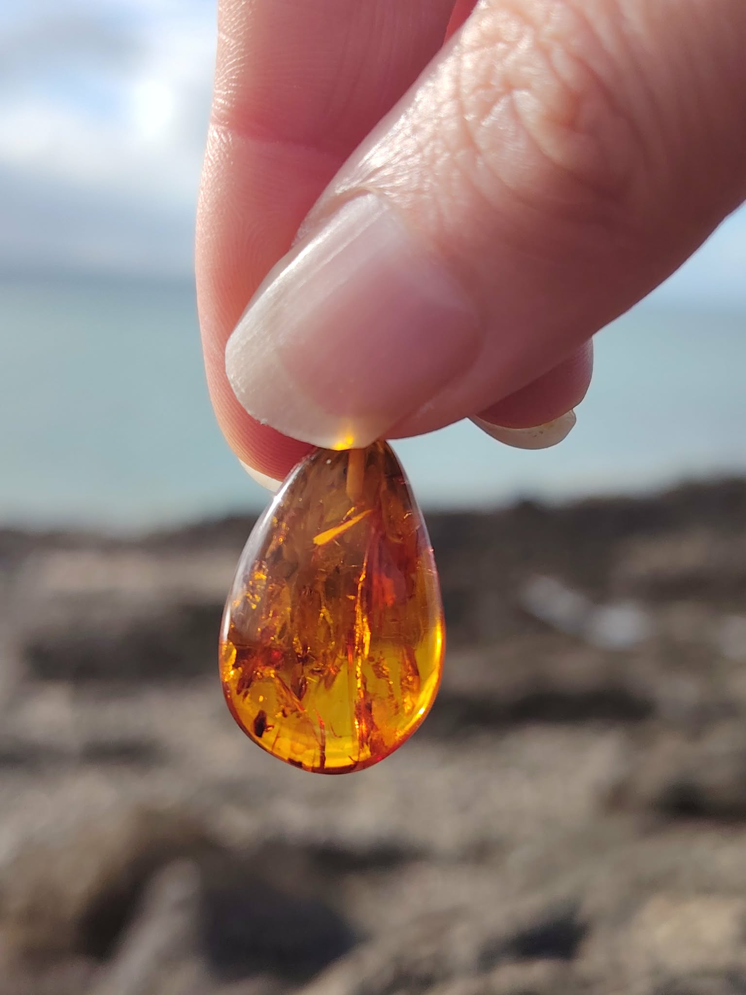 Goutte d’Ambre baltique tenue à la lumière en bord de mer breton, matière translucide miel doré, douceur intérieure et rayonnement personnel.