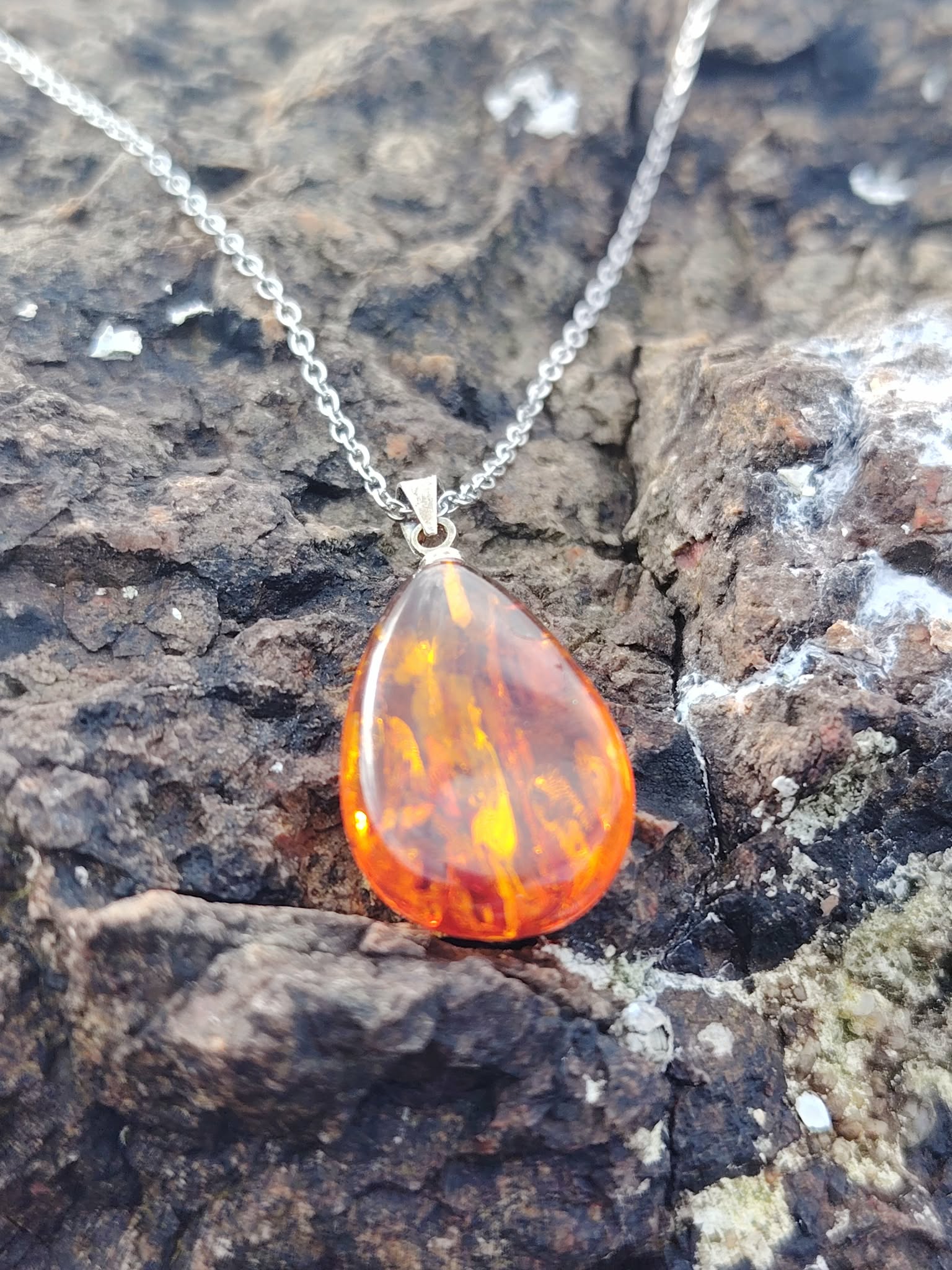 Pendentif Ambre baltique goutte sur roche sombre en Bretagne, reflets feu et miel, protection douce et chaleur réconfortante.