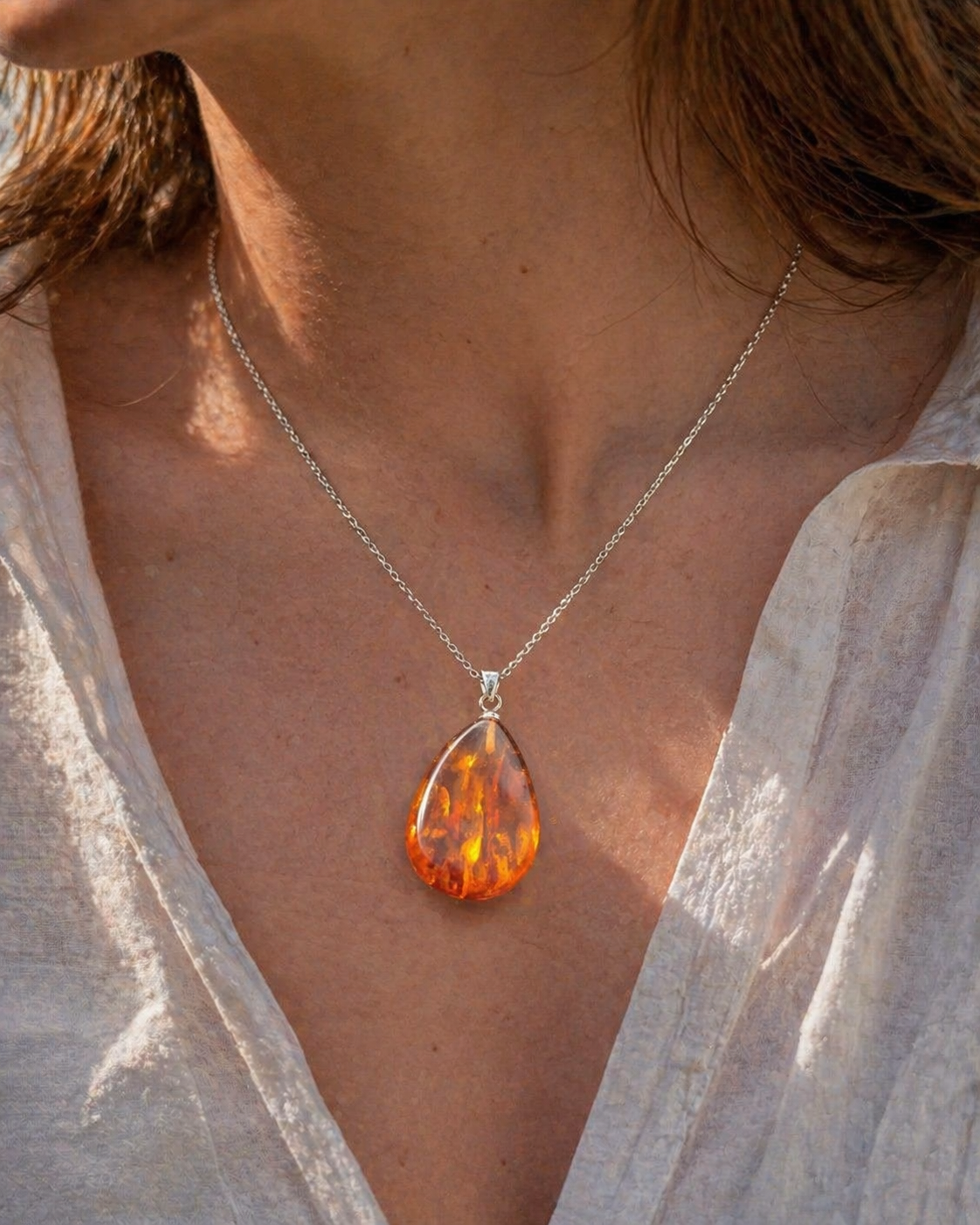 Pendentif Ambre baltique goutte porté sur chaîne argentée, bijou lumineux aux nuances cognac, réconfort émotionnel et énergie solaire.