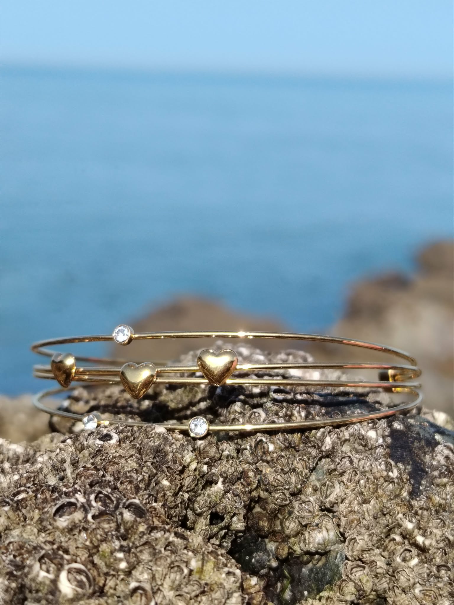 Bracelet jonc doré cœurs et strass en mise en scène naturelle, accessoire raffiné pour sublimer le poignet.