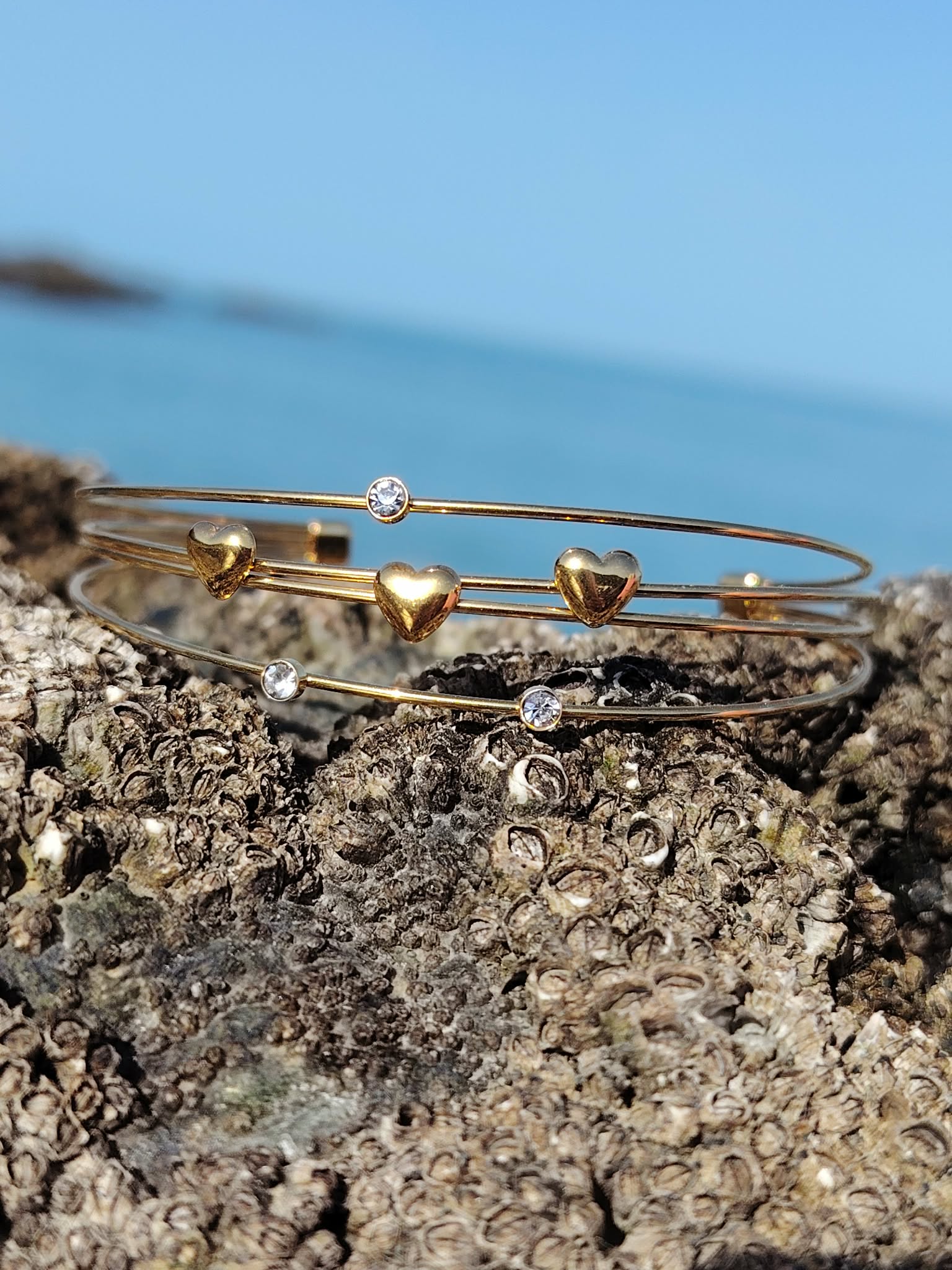Bijou de poignet doré quadruple fils, bracelet jonc ouvert orné de petits cœurs et strass, finition lumineuse.