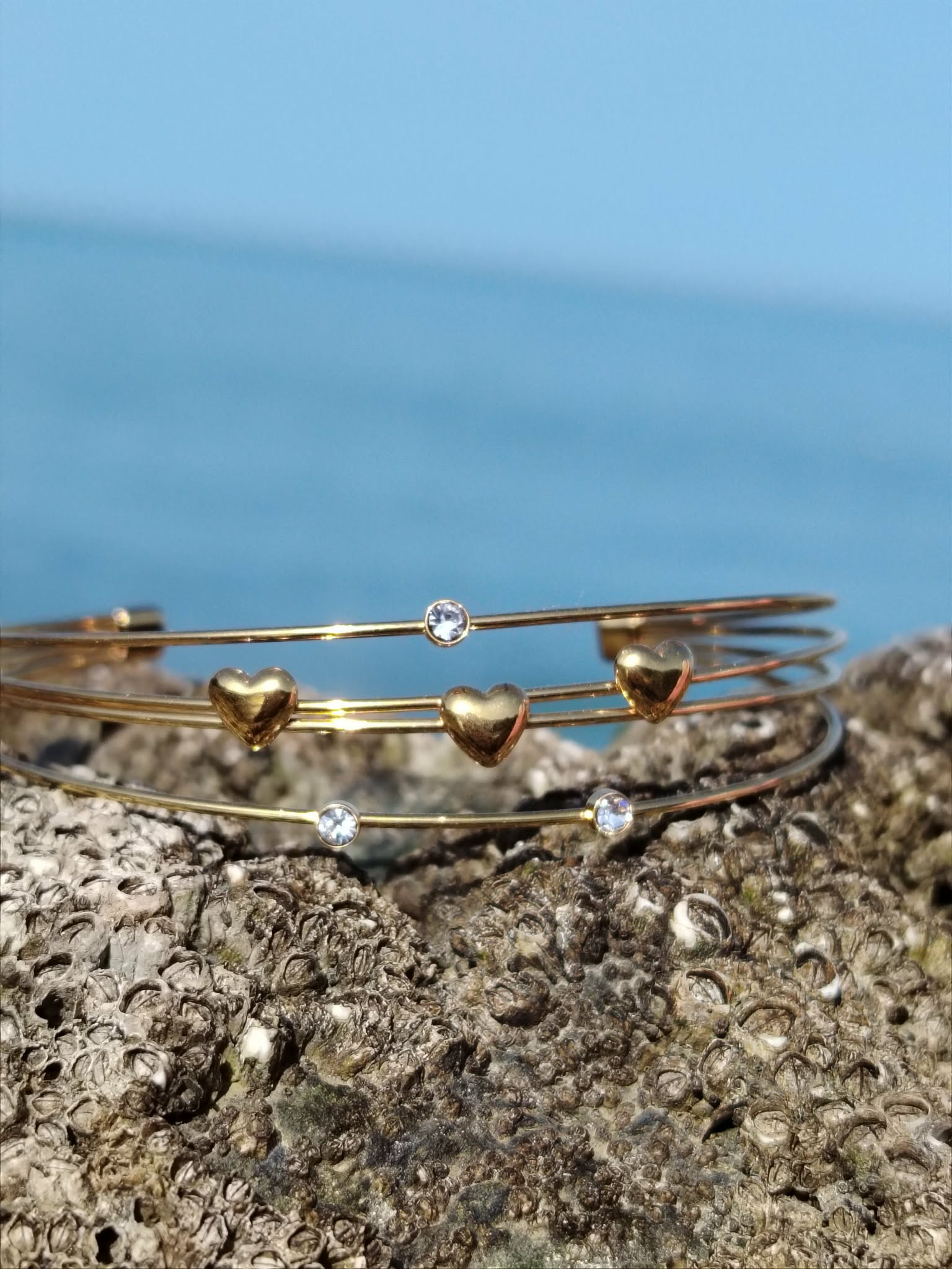 Bracelet jonc doré quadruple fils sur fond blanc, détails cœurs et strass lumineux, bijou ouvert élégant pour le poignet.