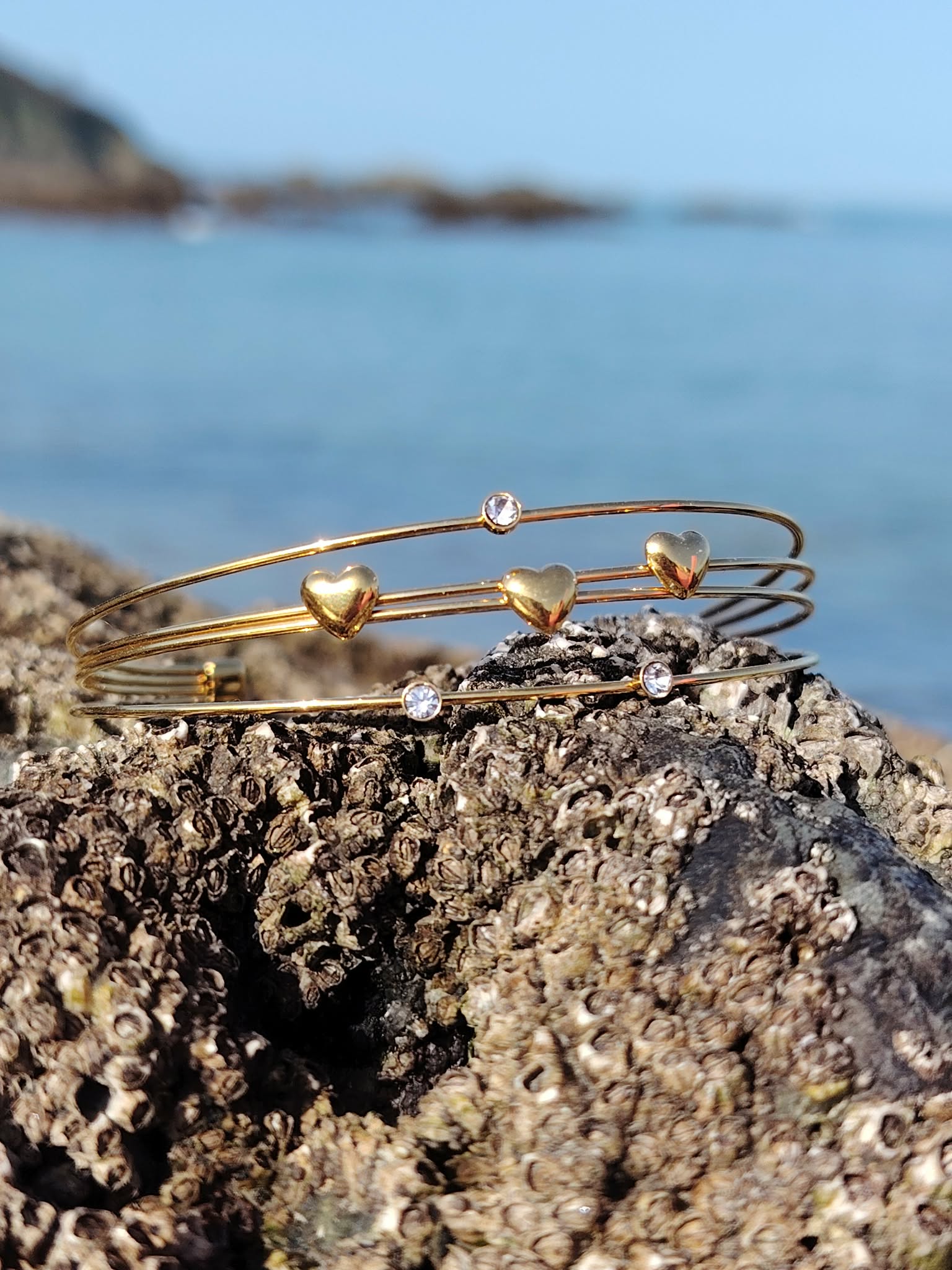 Bracelet doré à jonc ouvert sur décor doux, quatre fils fins avec cœurs et éclats de strass, style bohème chic.
