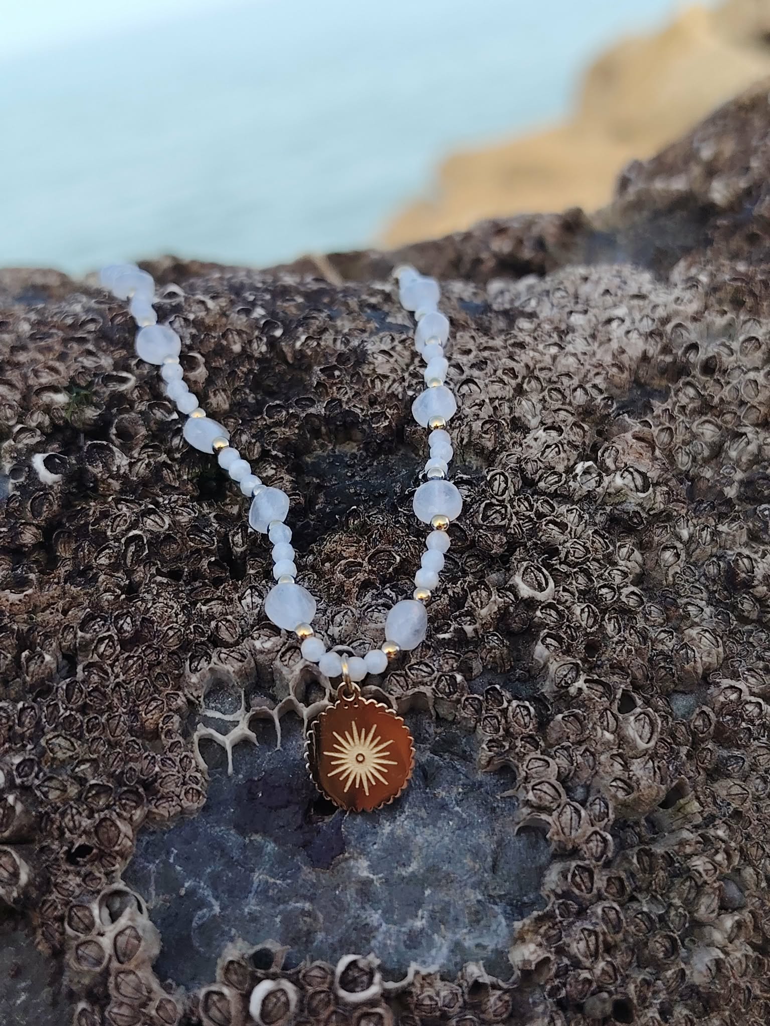 Collier Soleil Pierre de Lune sur roche en Bretagne, perles naturelles aux reflets nacrés et pendentif en acier inoxydable doré.