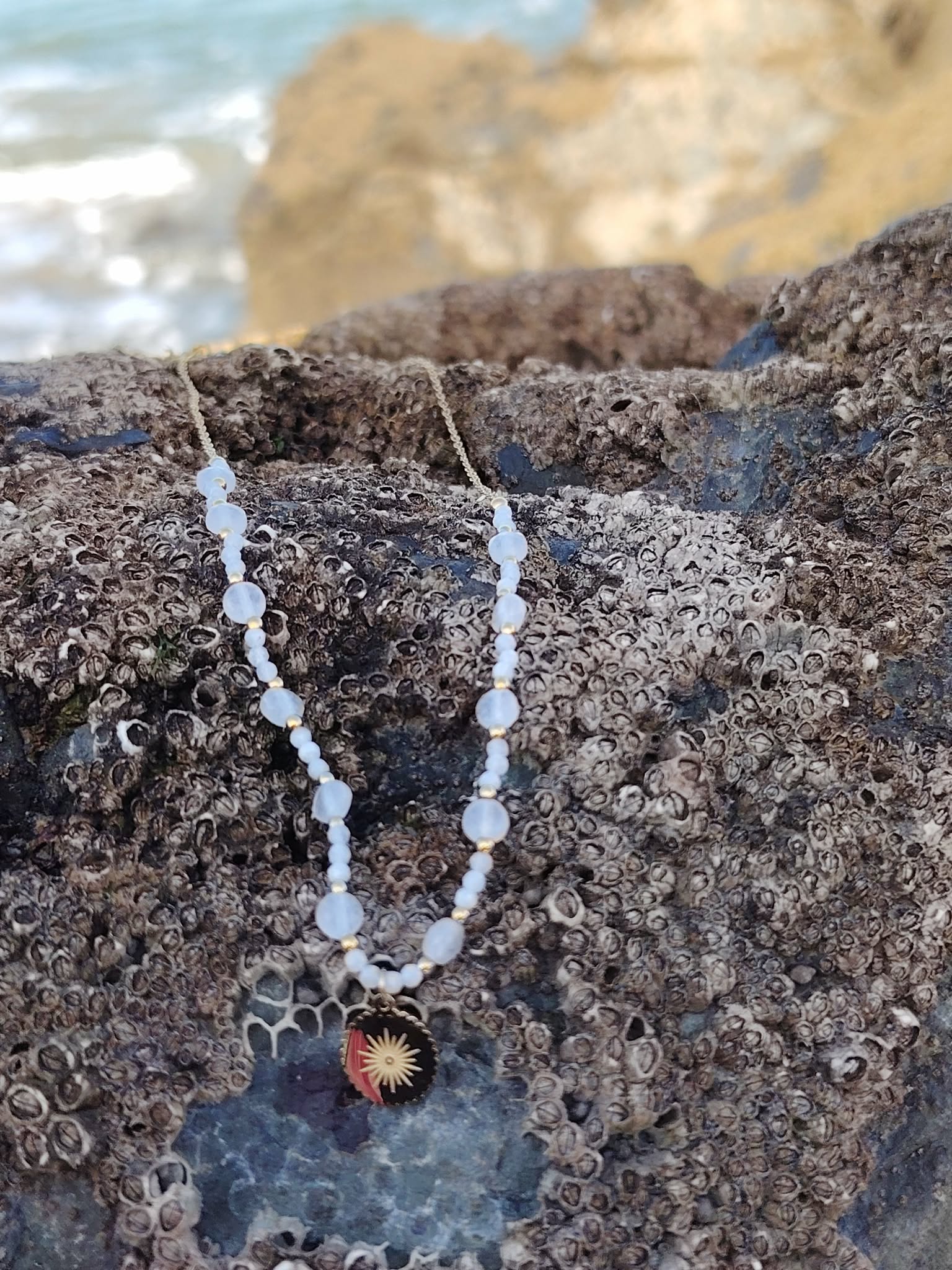 Collier en Pierre de Lune et pendentif soleil doré sur décor naturel, bijou lumineux associé à la féminité et l’apaisement.