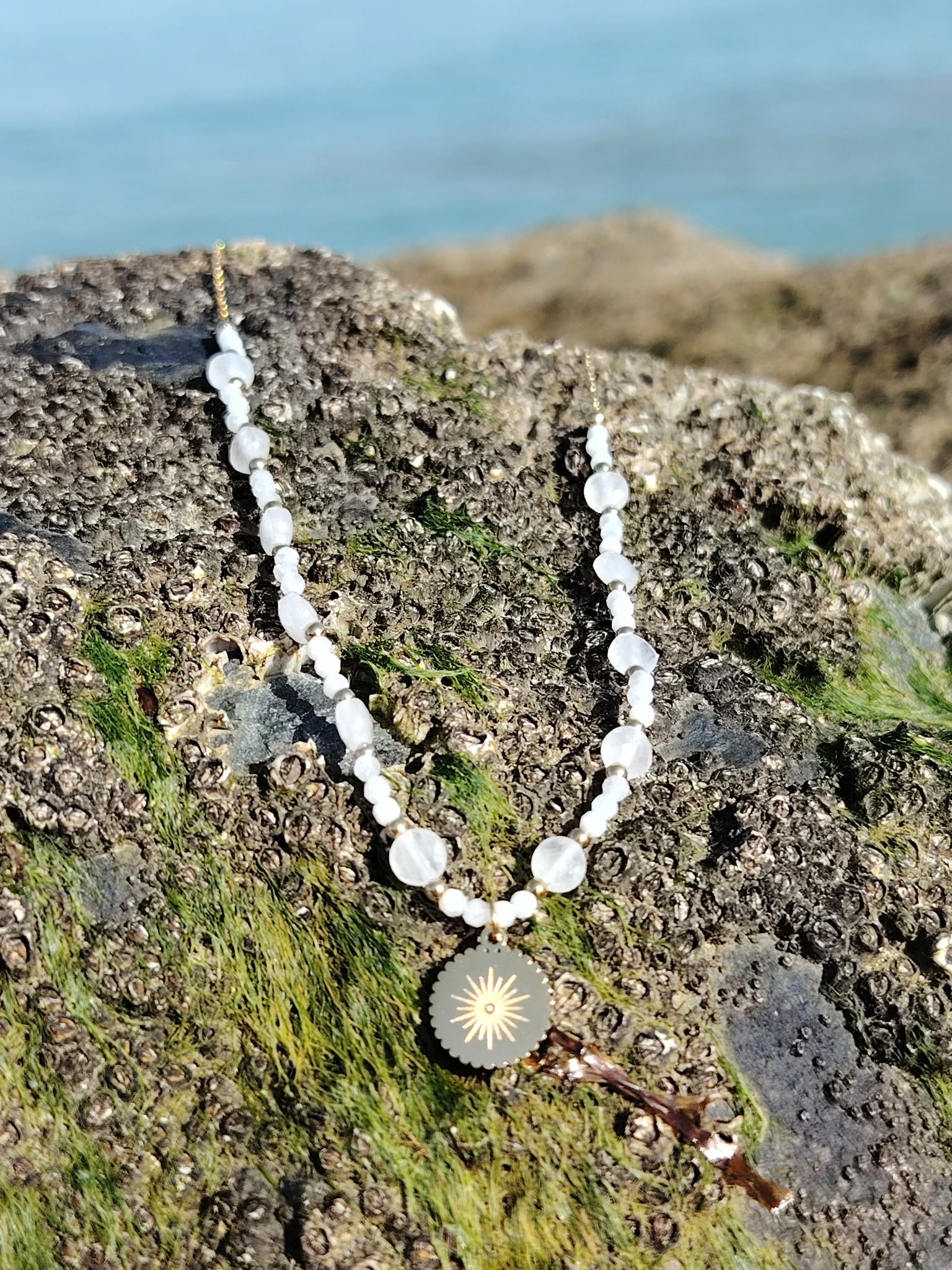 Gros plan sur collier Pierre de Lune avec soleil doré, perles nacrées et acier inoxydable, bijou féminin et solaire.