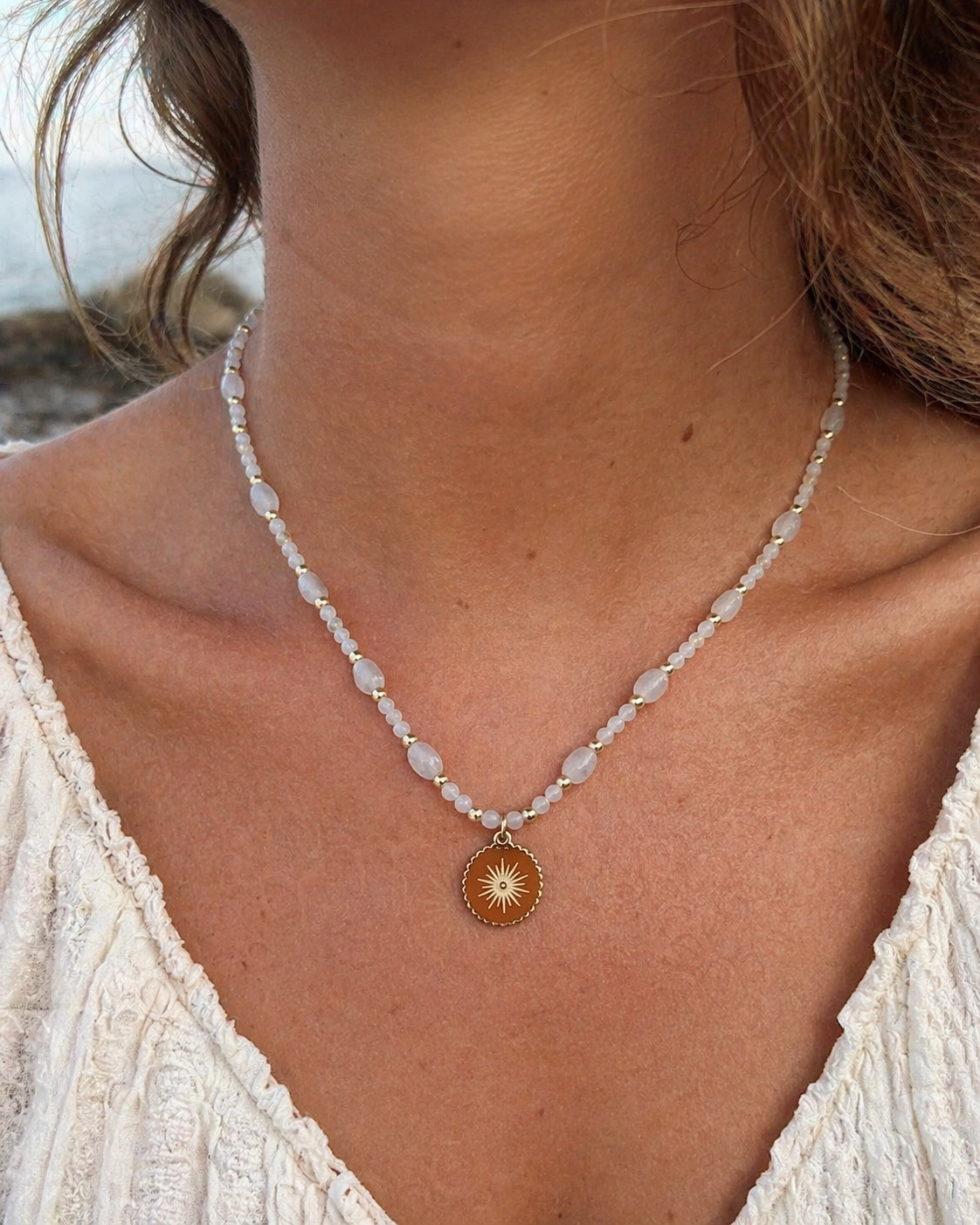 Collier Pierre de Lune porté au cou, pendentif soleil doré en acier inoxydable, reflets nacrés et style délicat.