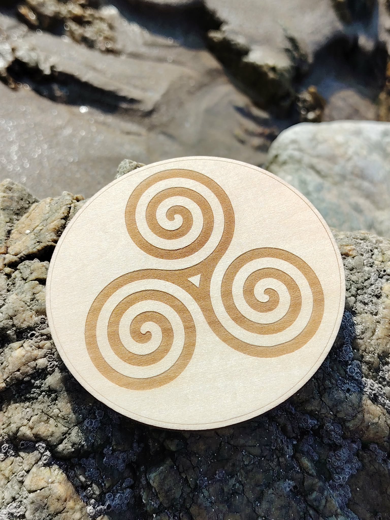 Plaque Triskell 10 cm sur rocher au bord de mer en Bretagne, motif celtique gravé pour équilibre et évolution.