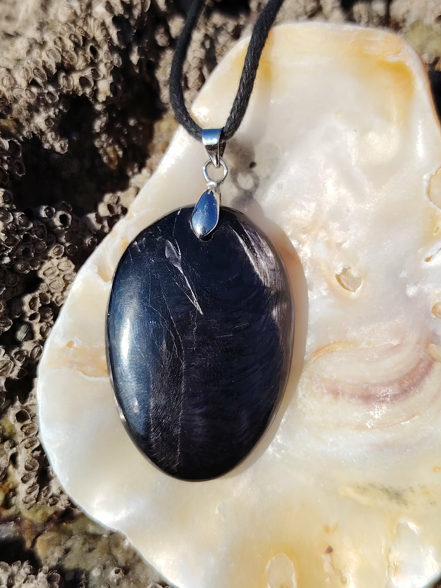 Pendentif Hyperstène ovale sur coquillage clair en Bretagne, pierre noire polie à reflets métallisés, calme mental et protection douce