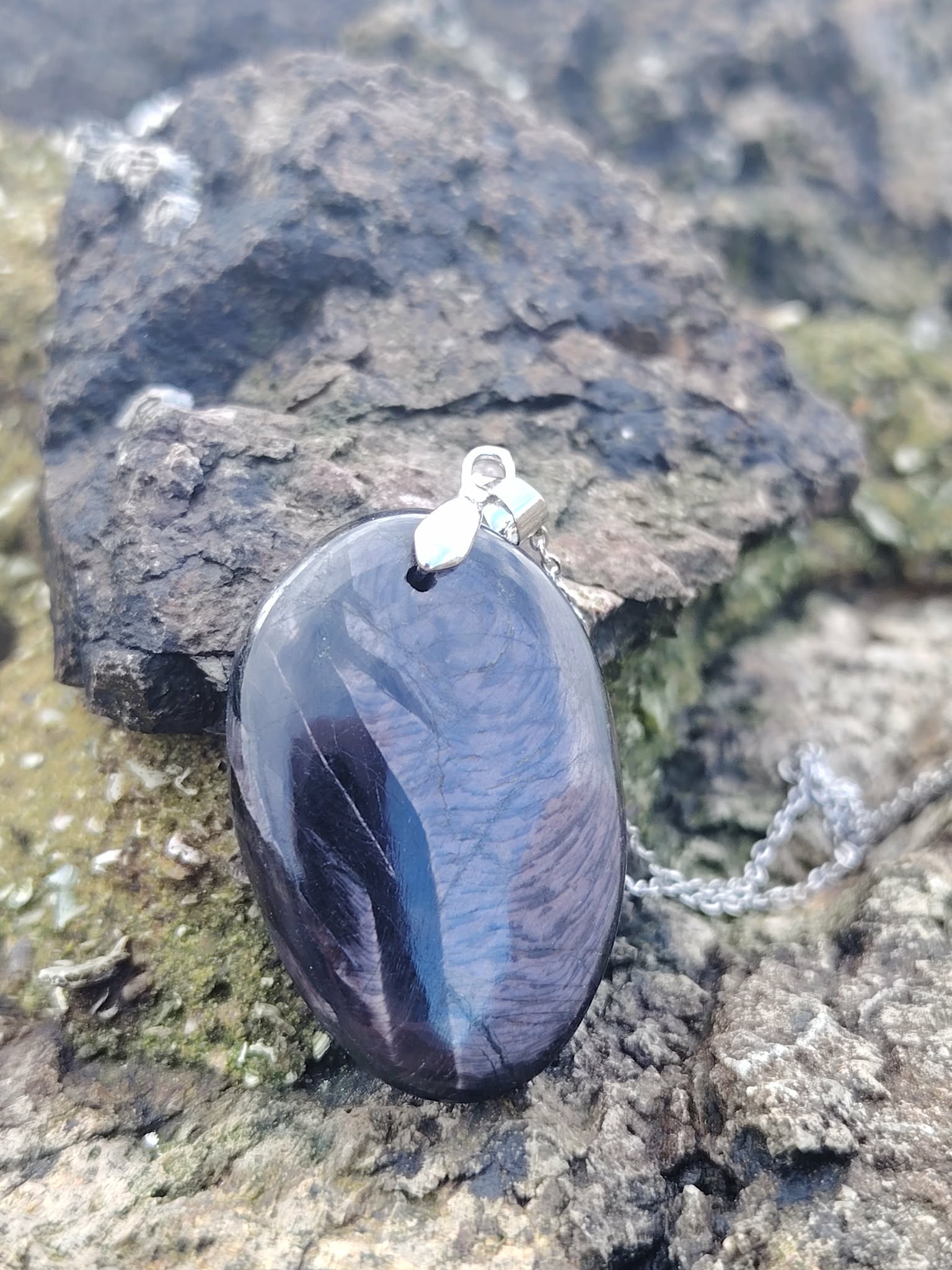 Pendentif Hyperstène sur rochers humides en Bretagne avec chaîne argentée, pierre naturelle pour ancrage, recul et stabilité intérieure