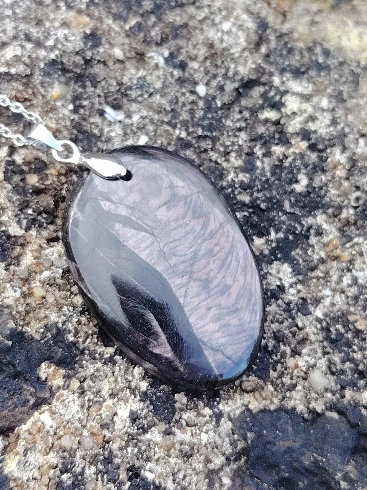 Pendentif Hyperstène ovale sur roche en Bretagne, pierre noire à reflets argentés, ancrage, protection symbolique et stabilité intérieure