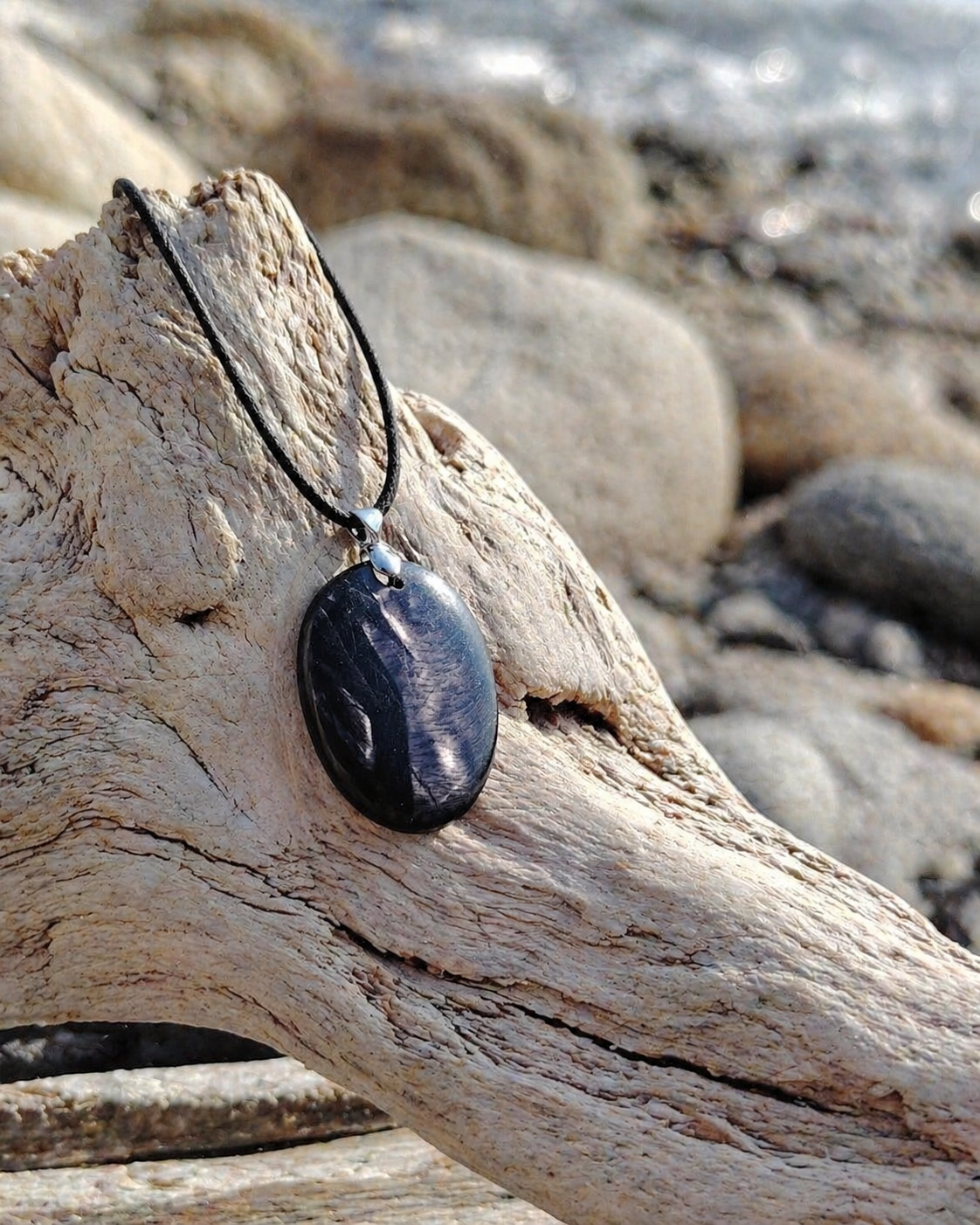 Pendentif Hyperstène posé sur bois flotté en Bretagne face à la mer, bijou en pierre naturelle pour ancrage et force intérieure