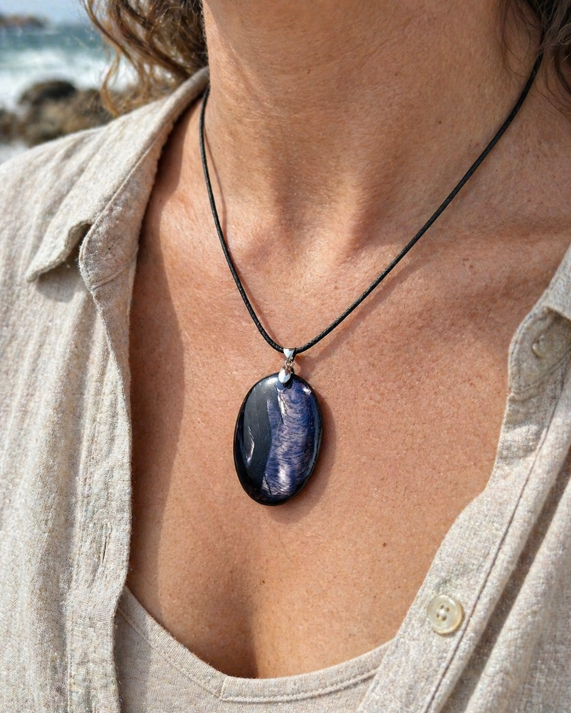 Pendentif Hyperstène porté sur peau en lumière naturelle au bord de mer en Bretagne, pierre de calme intérieur et de protection douce