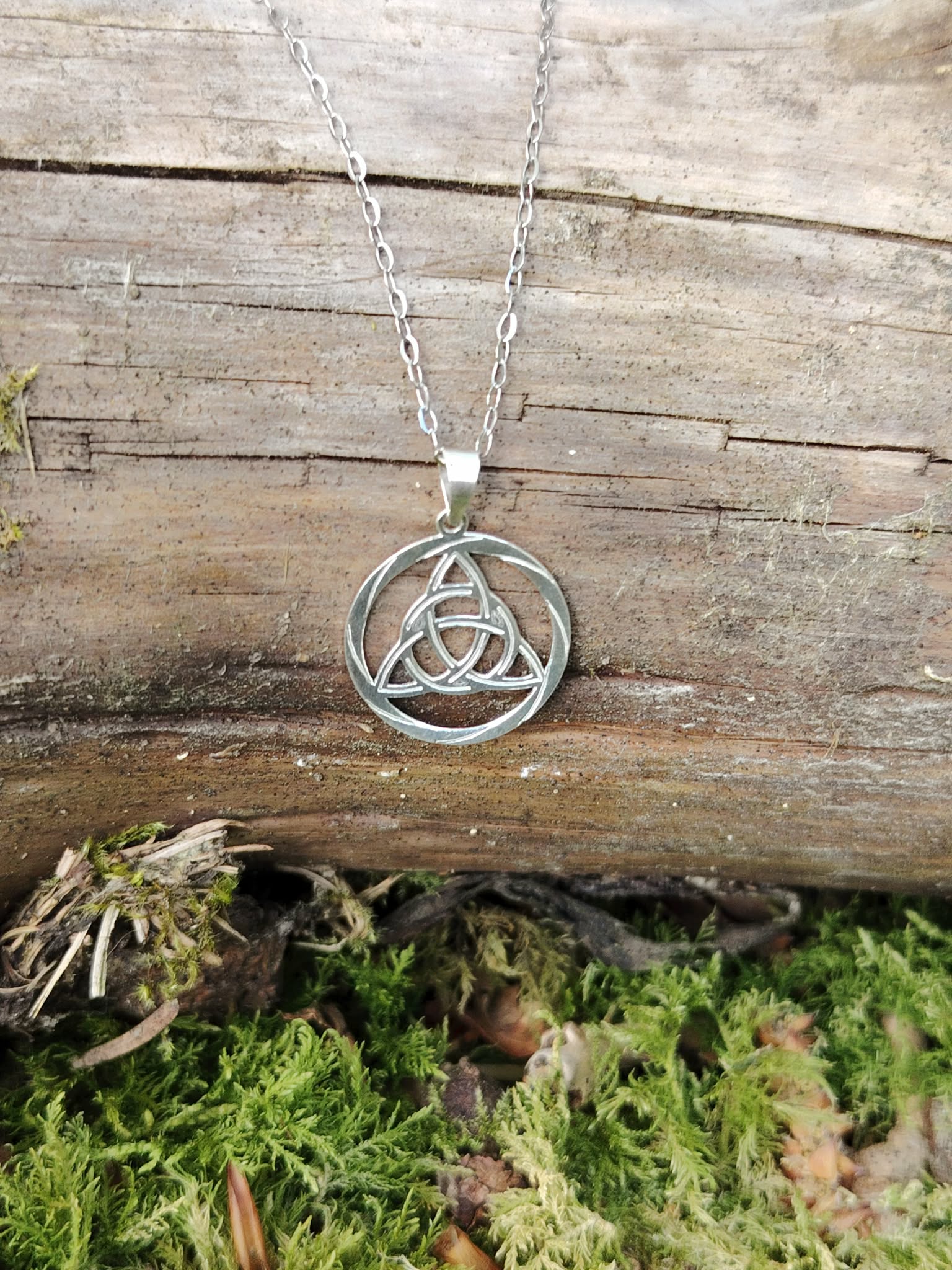 Pendentif Triquetra rond en argent 925 sur décor naturel en Bretagne, bijou celtique ajouré au motif entrelacé.