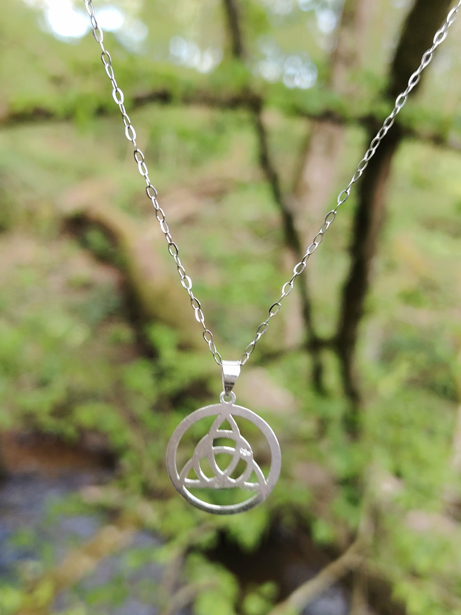 Pendentif Triquetra en argent 925 posé sur mousse en forêt bretonne, bijou celtique de protection et de recentrage.
