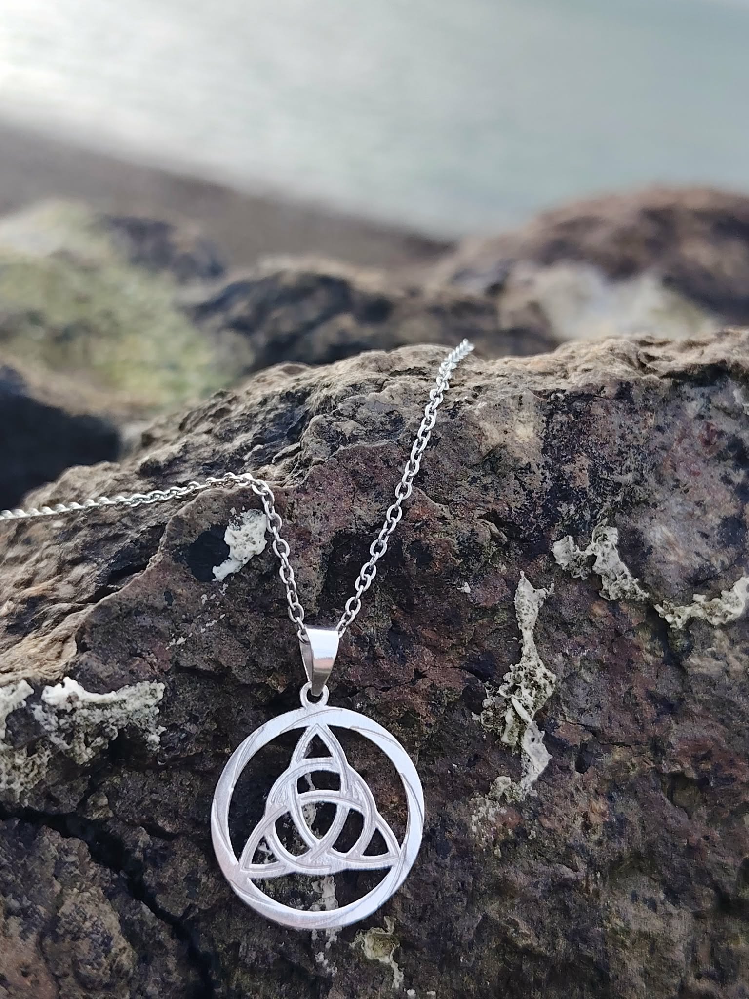 Gros plan sur pendentif Triquetra rond en argent 925 en Bretagne, médaillon celtique ajouré aux entrelacés délicats.