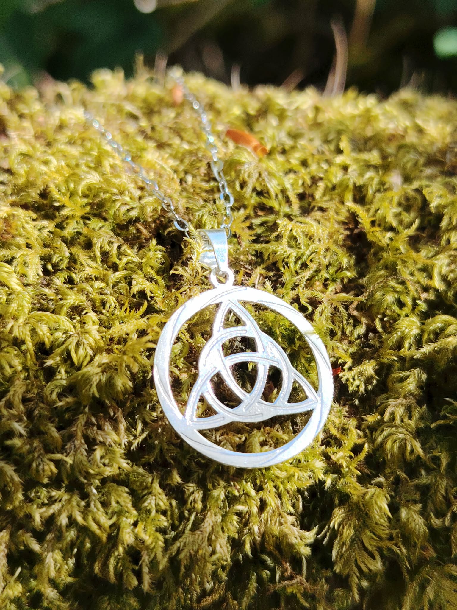 Pendentif Triquetra en argent 925 sur fond minéral en Bretagne, bijou ajouré inspiré des traditions celtiques et de la protection.