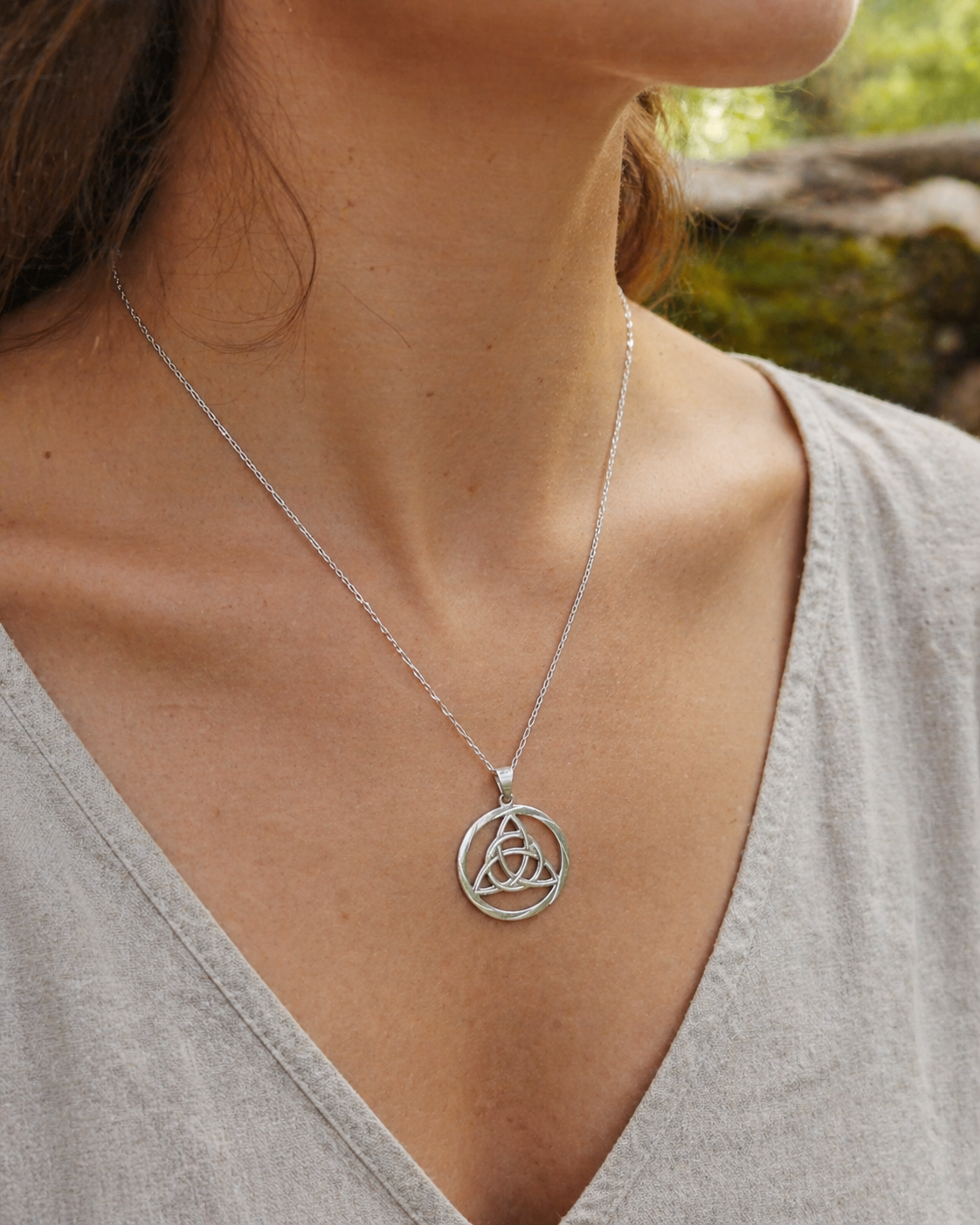 Pendentif Triquetra rond en argent 925 porté sur décolleté clair, collier celtique ajouré en lumière naturelle.