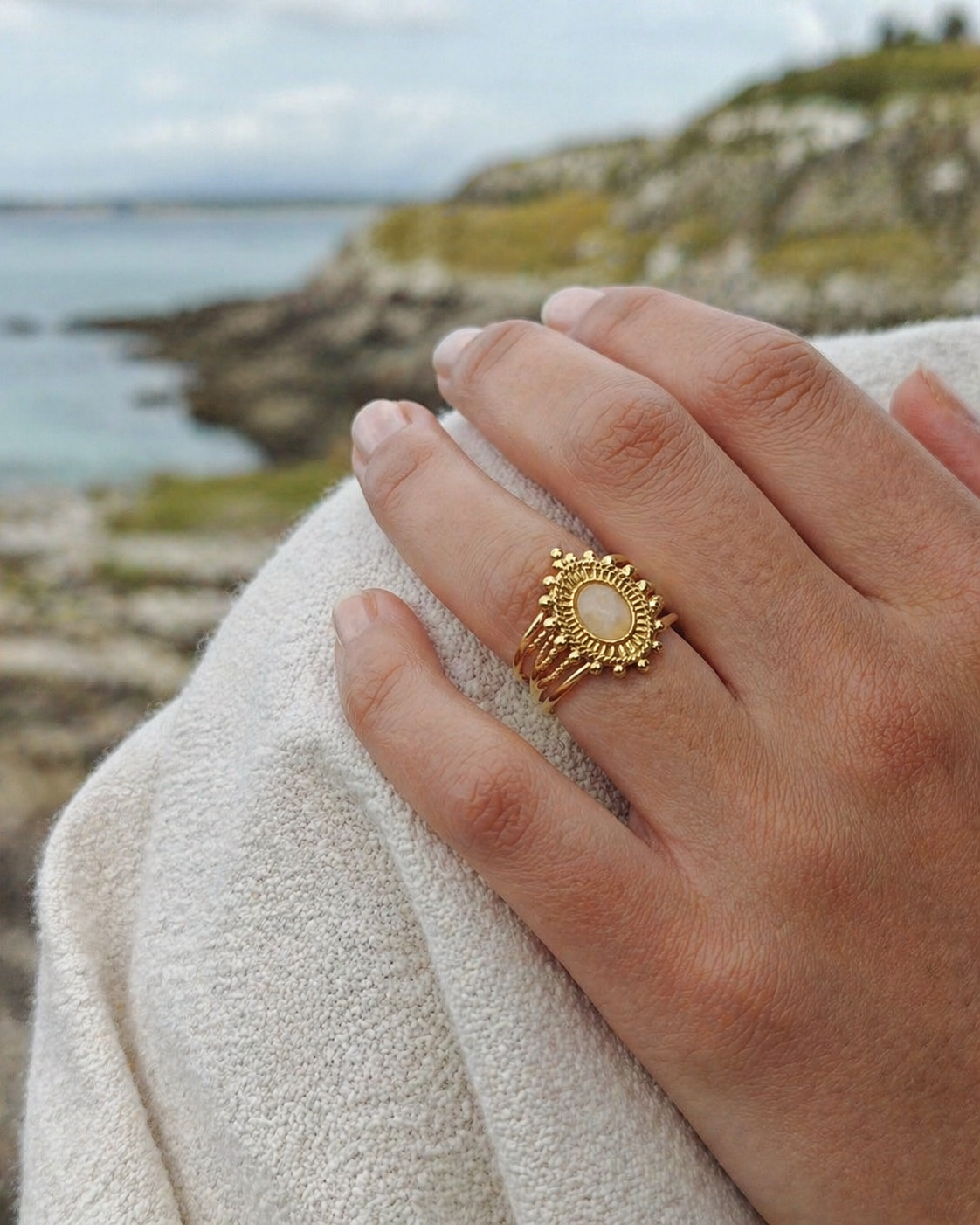 Bague dorée ajustable portée à la main au bord de mer en Bretagne, pierre de soleil rosée au style élégant et énergie positive