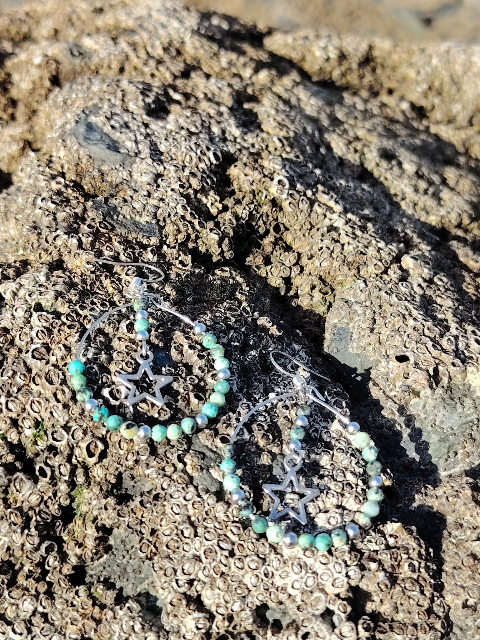 Boucles d’oreilles en turquoise africaine facettée posées sur pierre naturelle en Bretagne, créoles en acier inoxydable avec perles marbrées vert bleuté et breloques étoiles argentées.